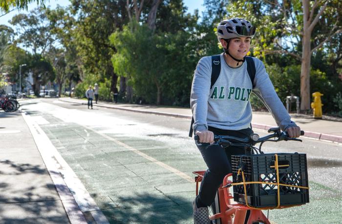 A Cal Poly student wearing a helmet while riding a bike in the bike lane.  