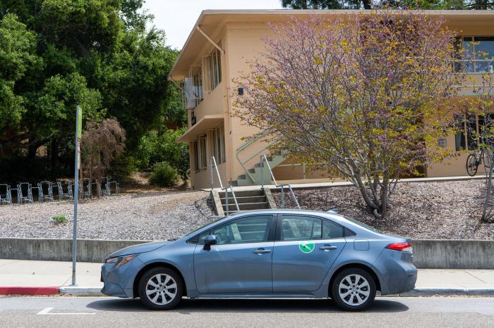 A blue Zipcar parked outside of a dorm building.