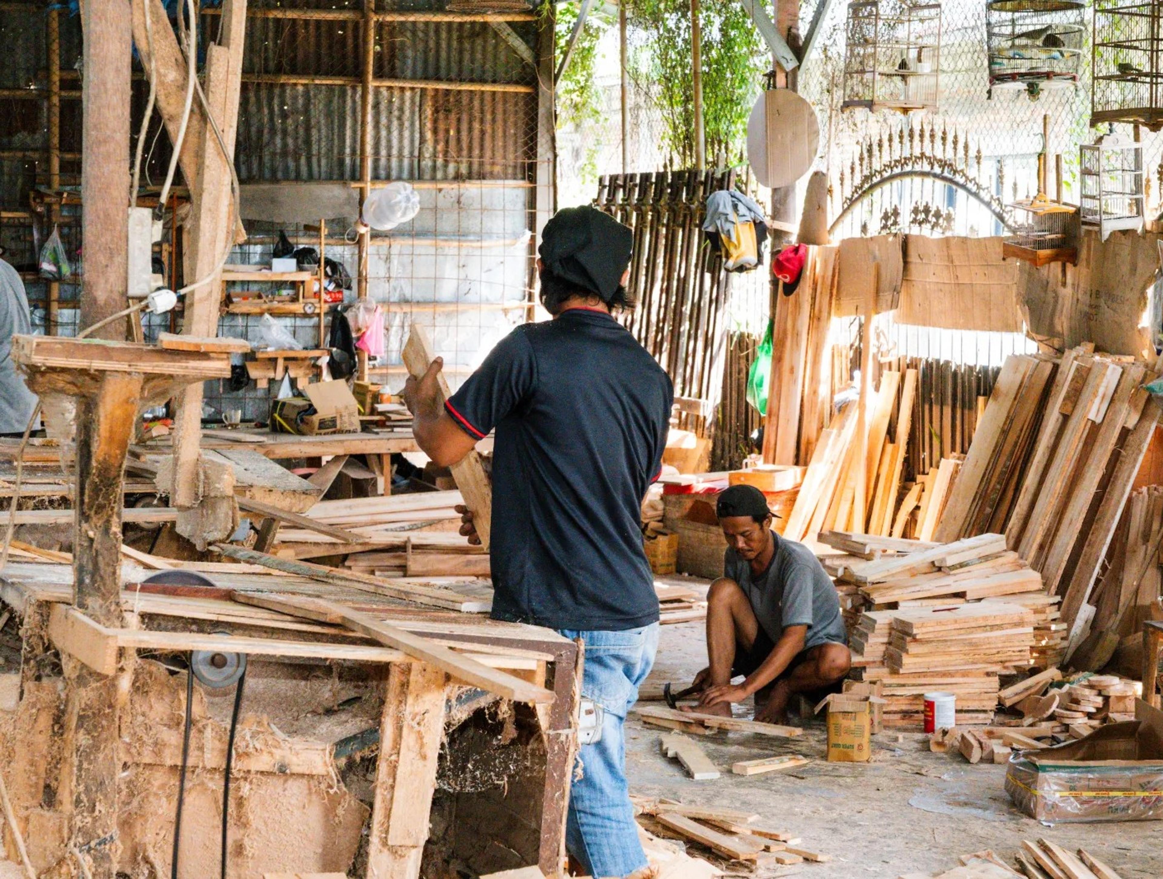 Perajin memotong dan menyusun papan kayu untuk rangka sofa di workshop Emerald
