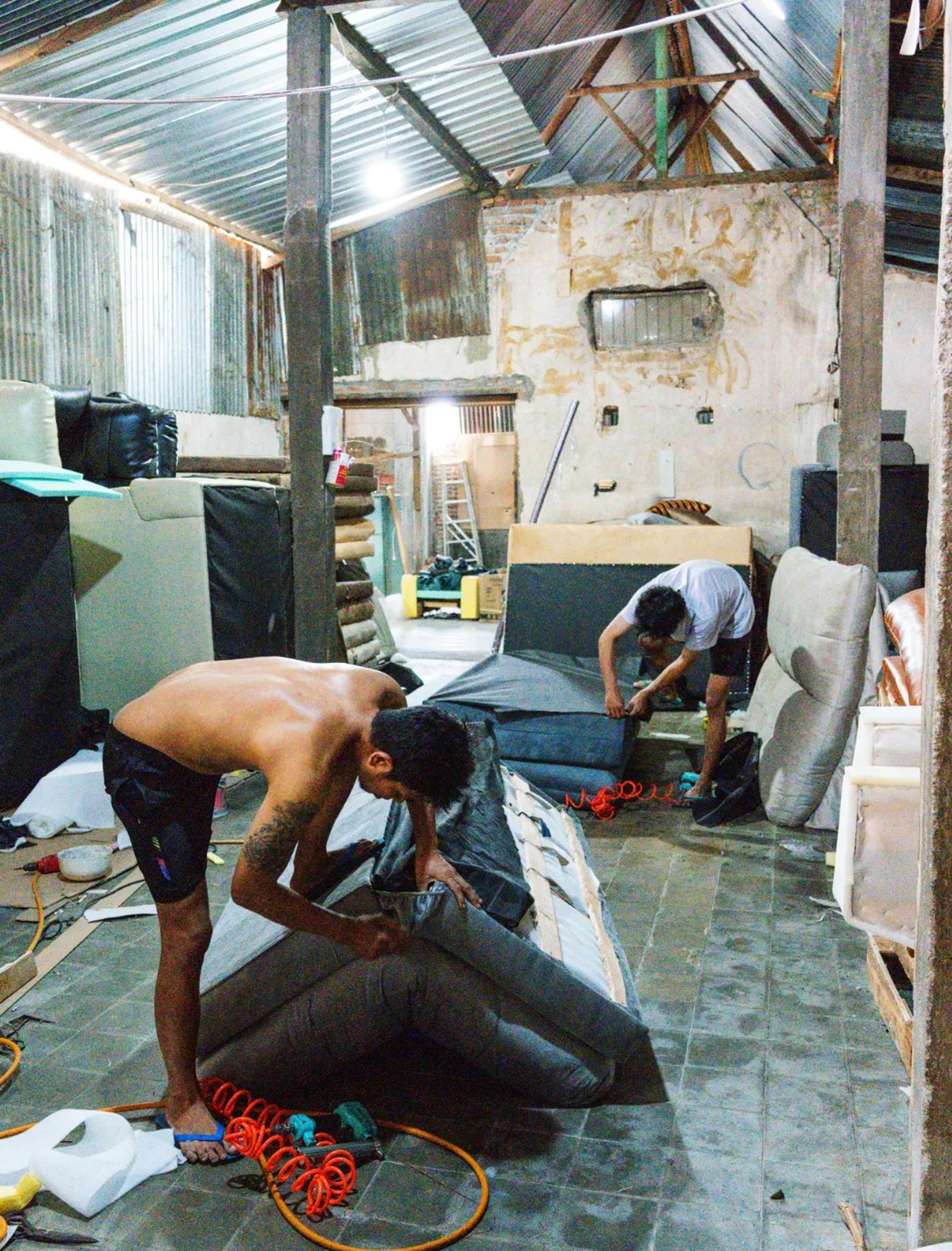 Perajin memasang kain pelapis pada sofa di workshop Emerald