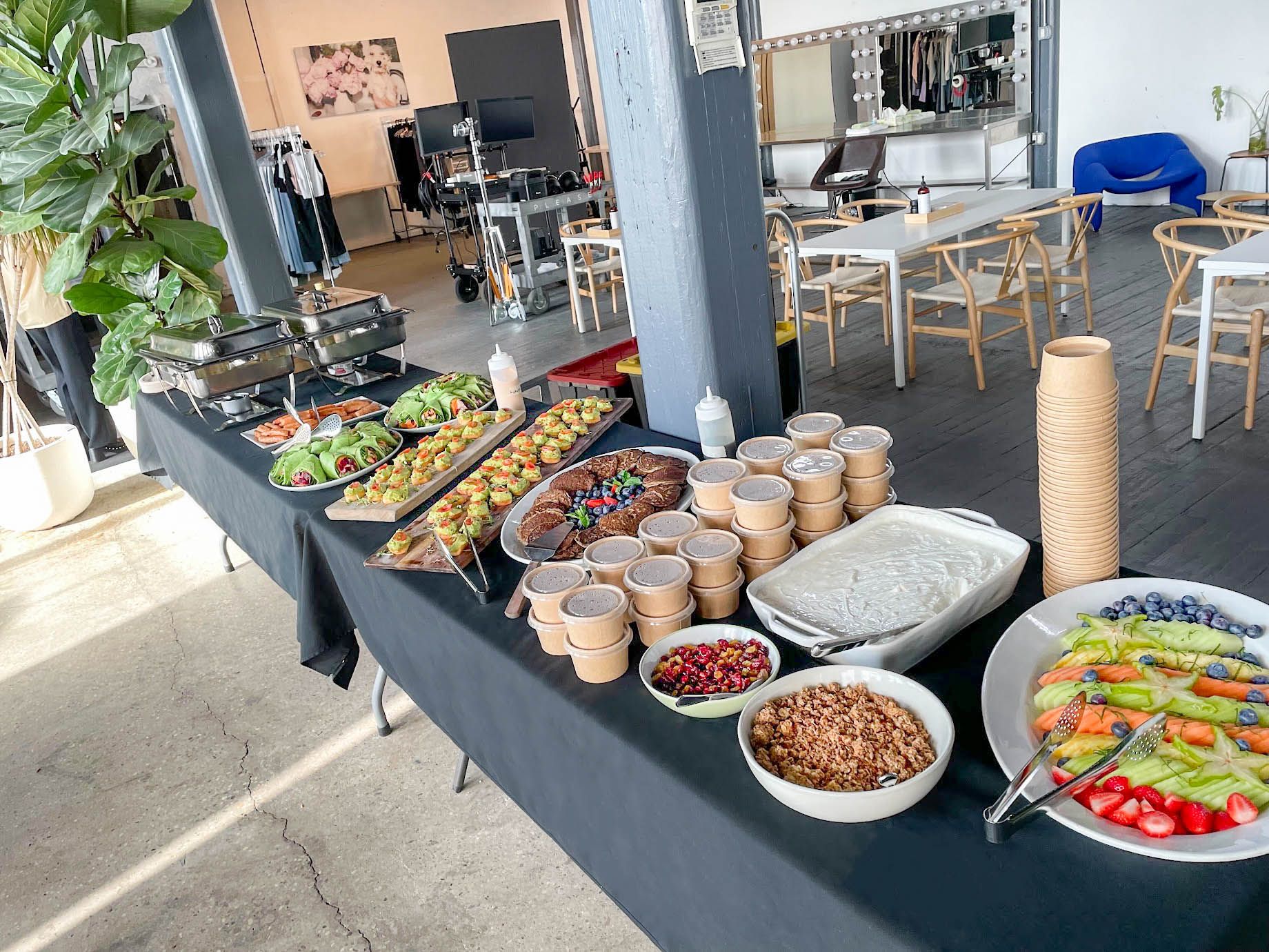 Catering lunch buffet with salads, wraps, fruit, and plated appetizers in a studio space.