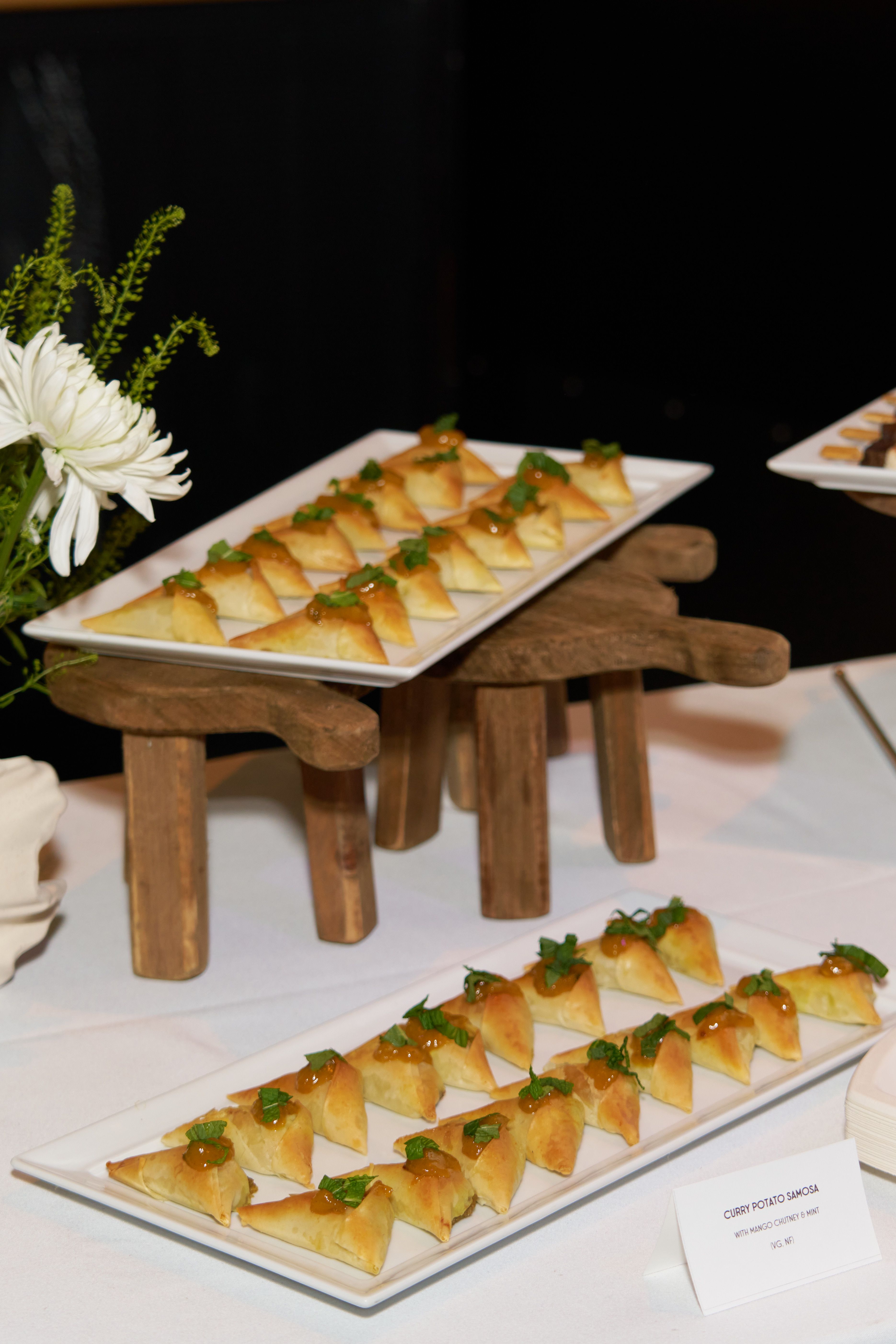 Catering display of curry potato samosa hors d'oeuvres served with mango chutney and mint.
