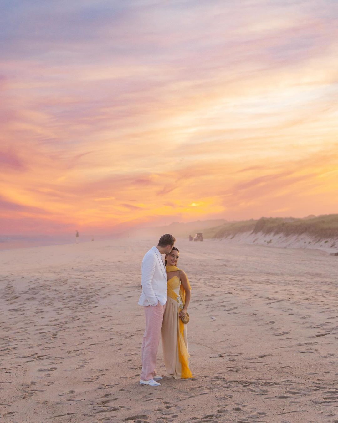 Couple standing on a beach at sunset during a Hamptons-style wedding celebration.