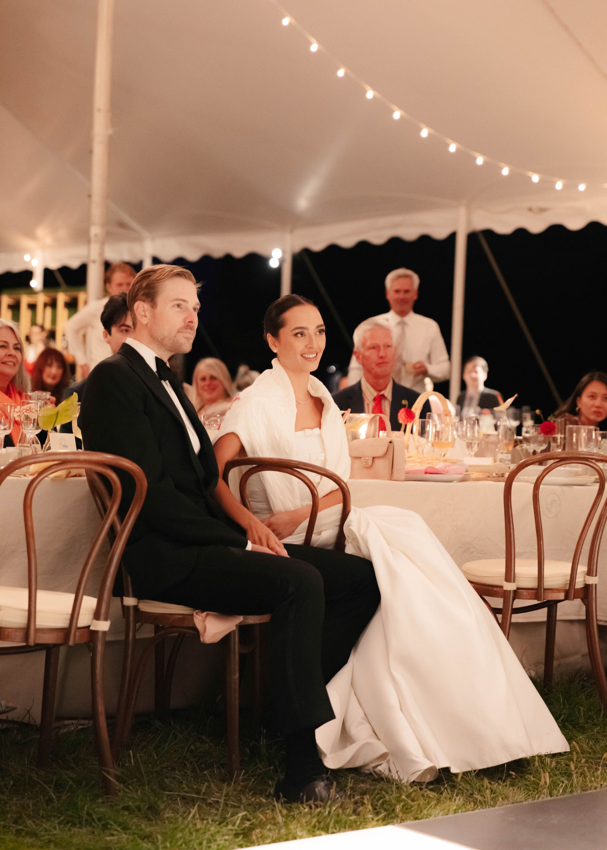Bride and groom seated at their wedding reception under a tent with catered dinner service.