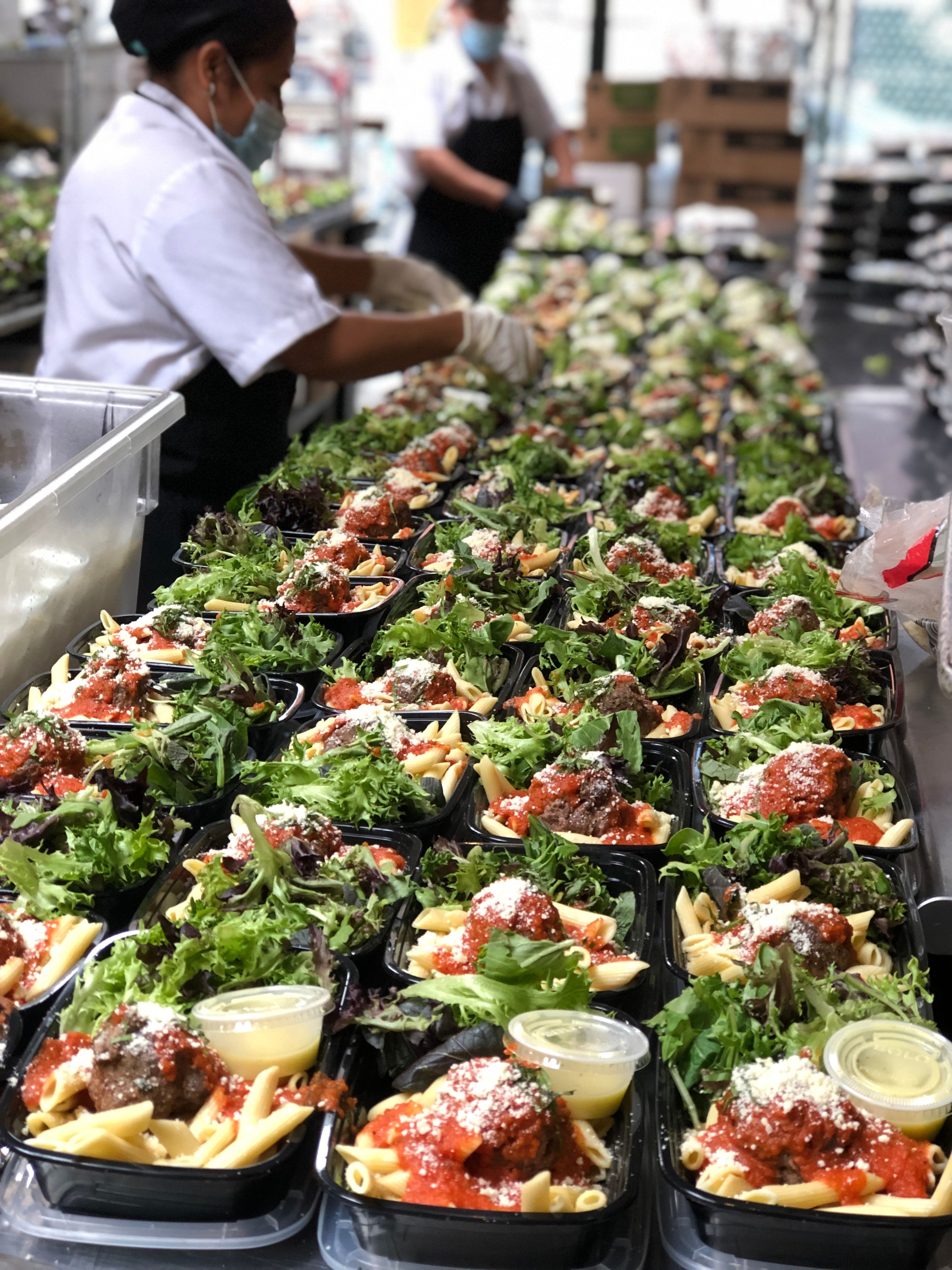 Catering team preparing hundreds of packaged pasta meals for emergency food response.