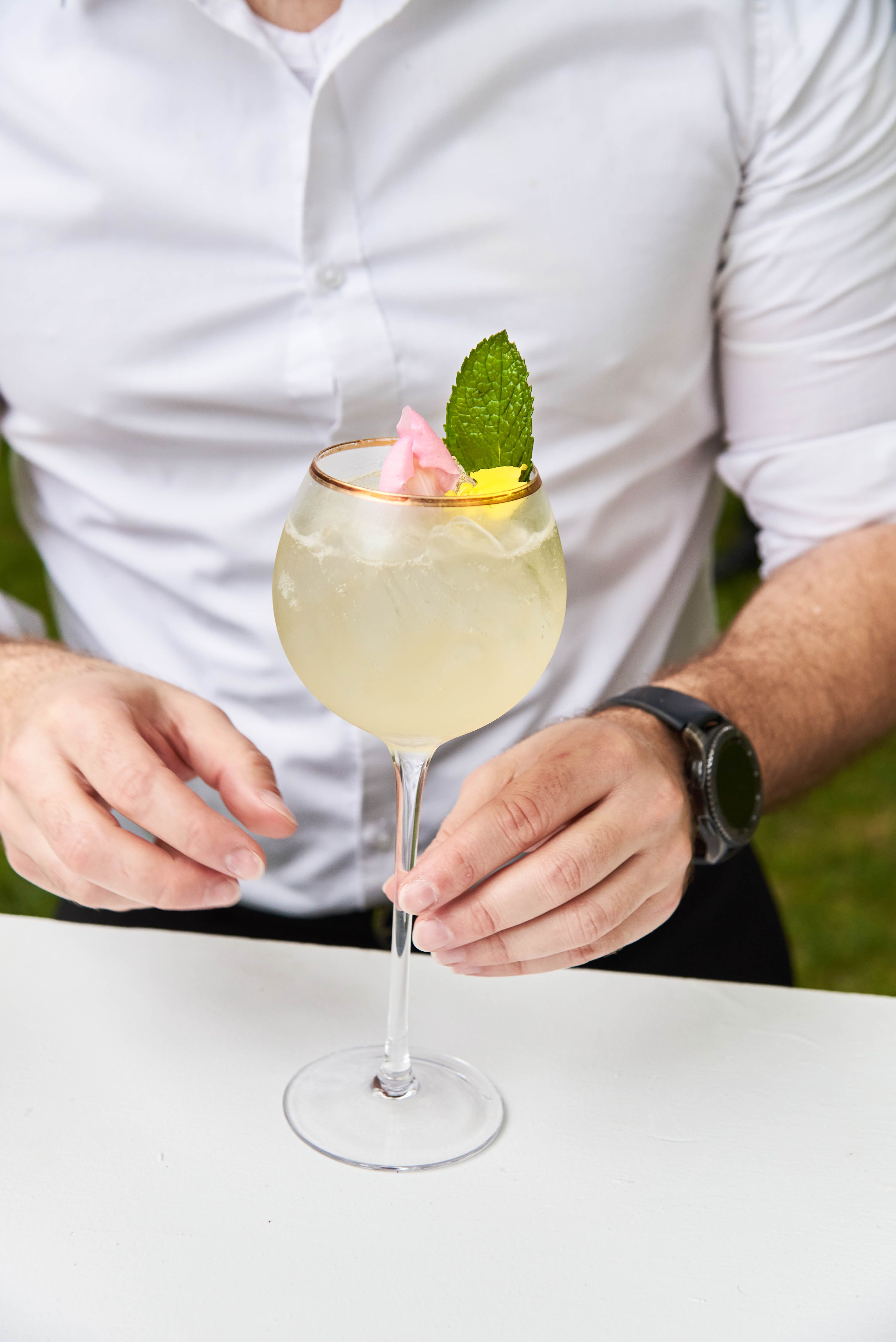 Bartender presenting a signature cocktail with fresh garnish during event catering service.