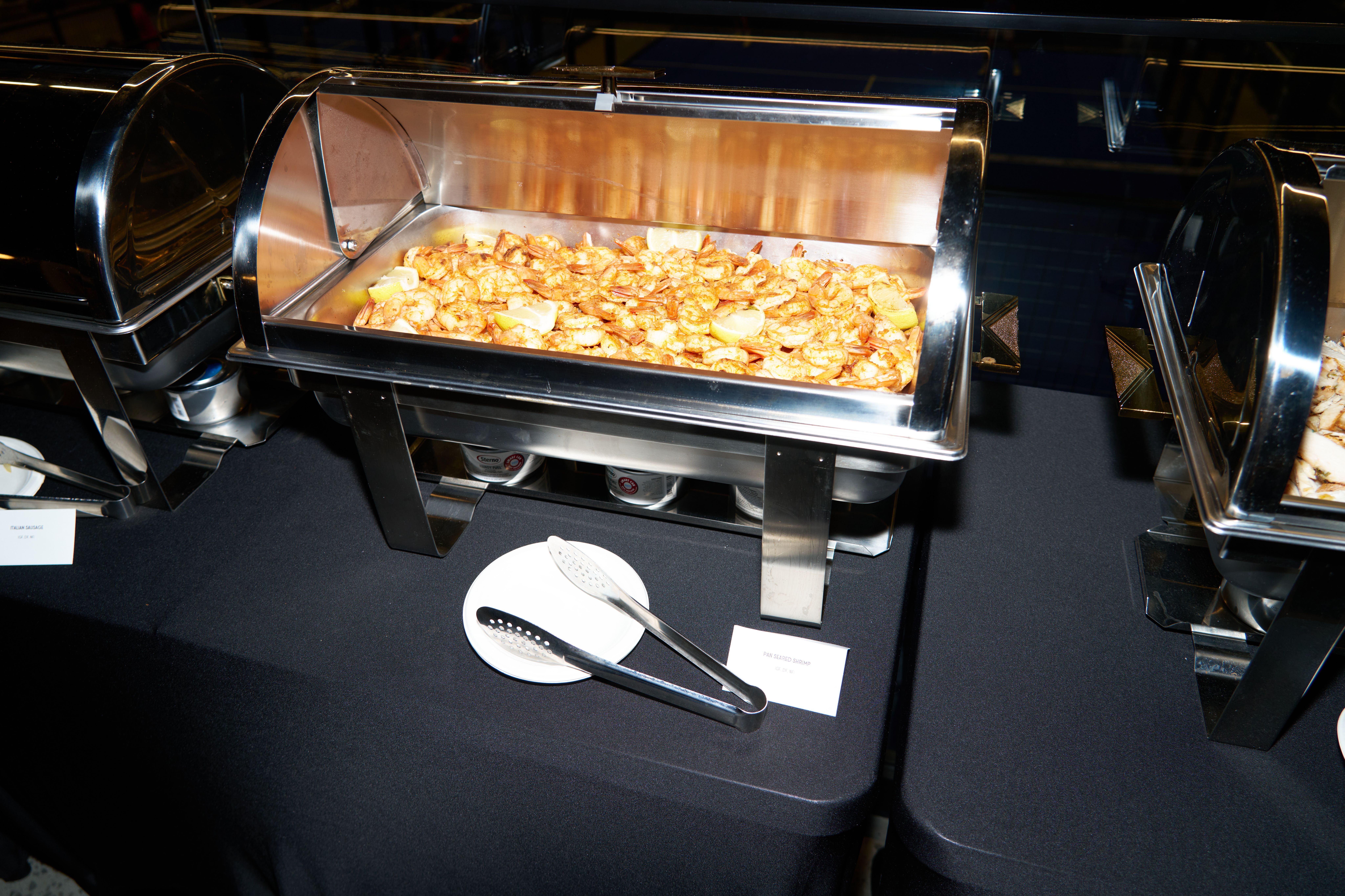 Buffet catering station with hot food trays and serving utensils at a corporate event.
