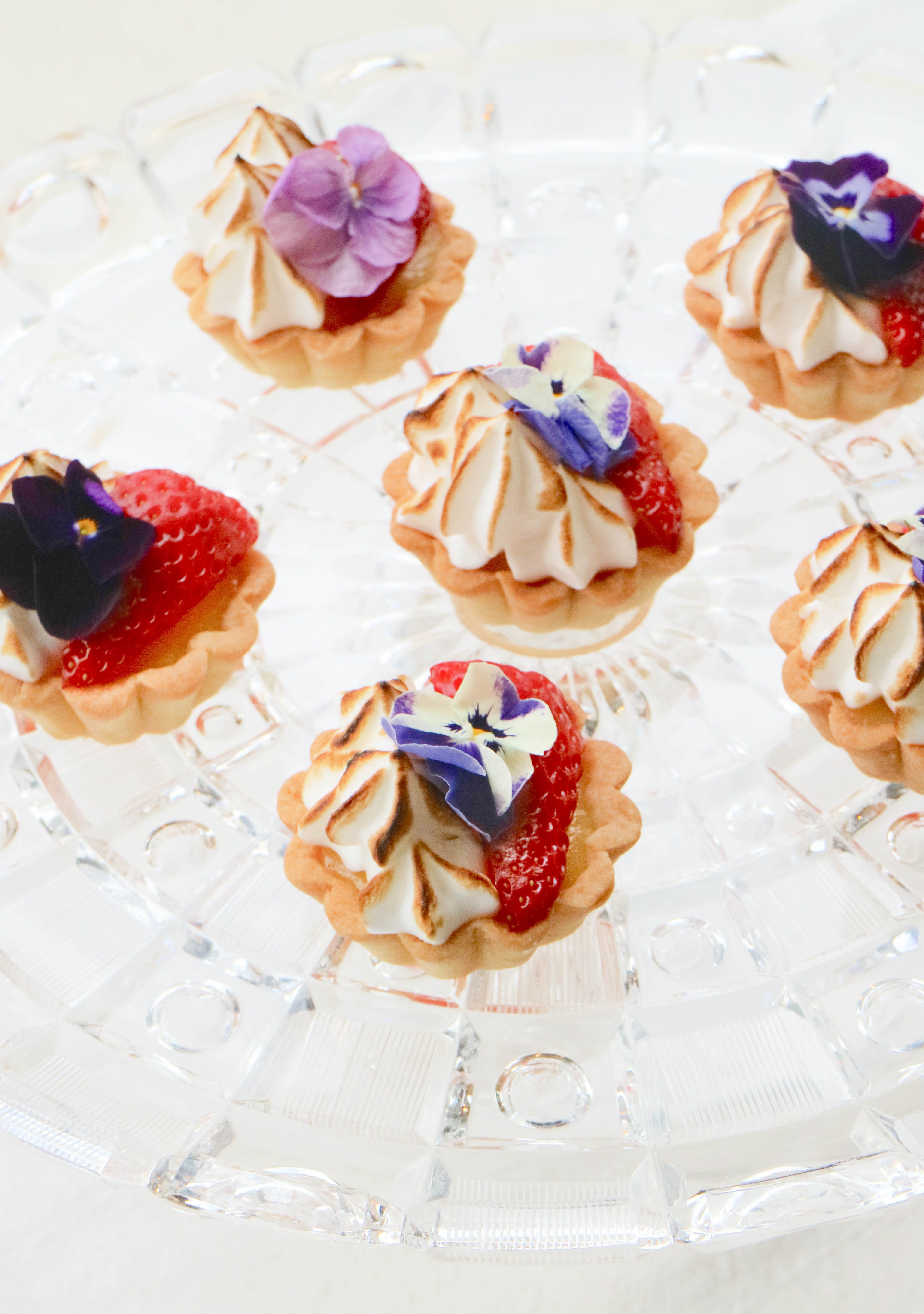 Mini wedding dessert tartlets with strawberries, toasted meringue, and edible flowers served at a catered reception.