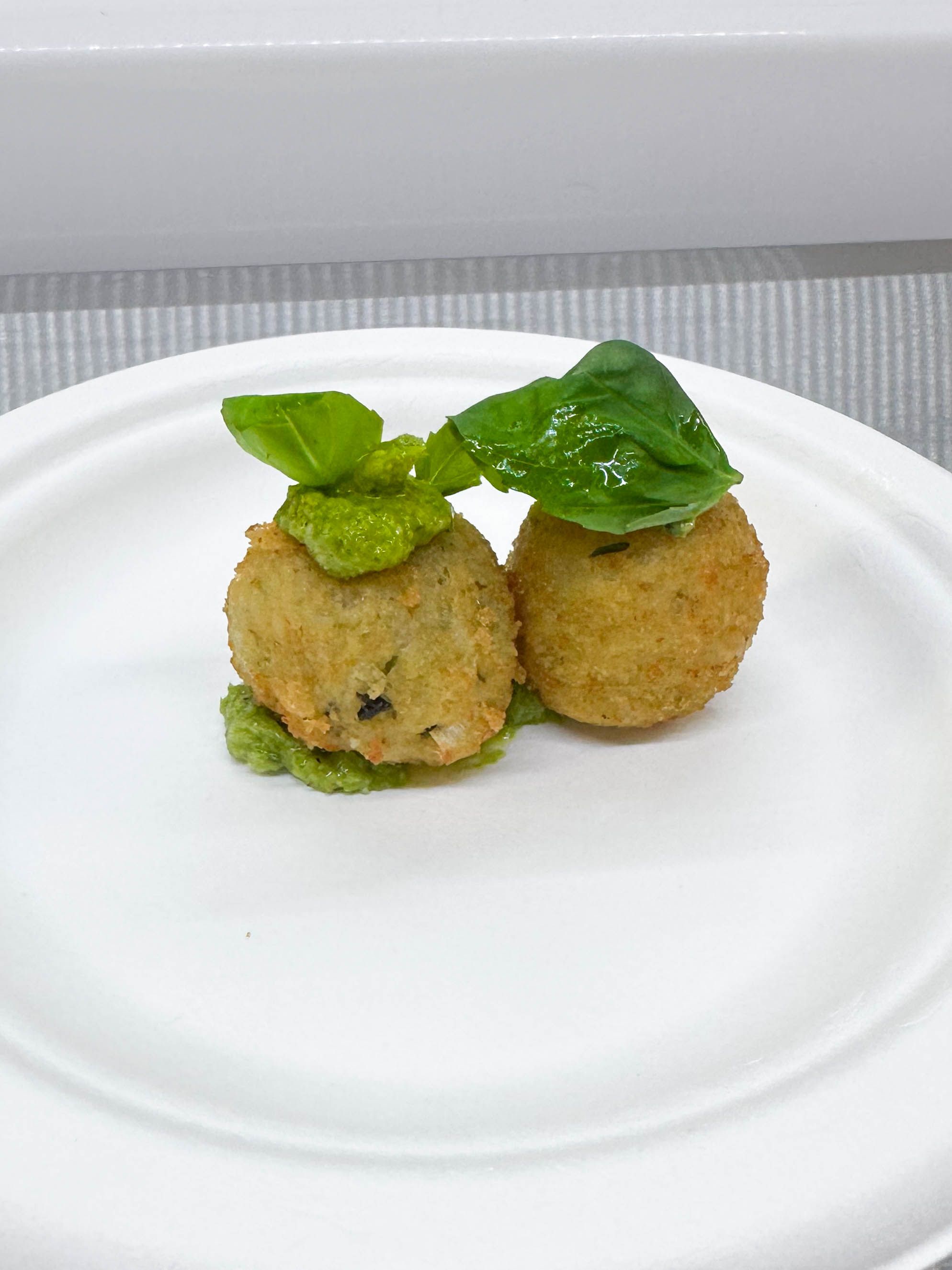 Crispy arancini appetizer topped with basil pesto served as a passed bite for event catering.