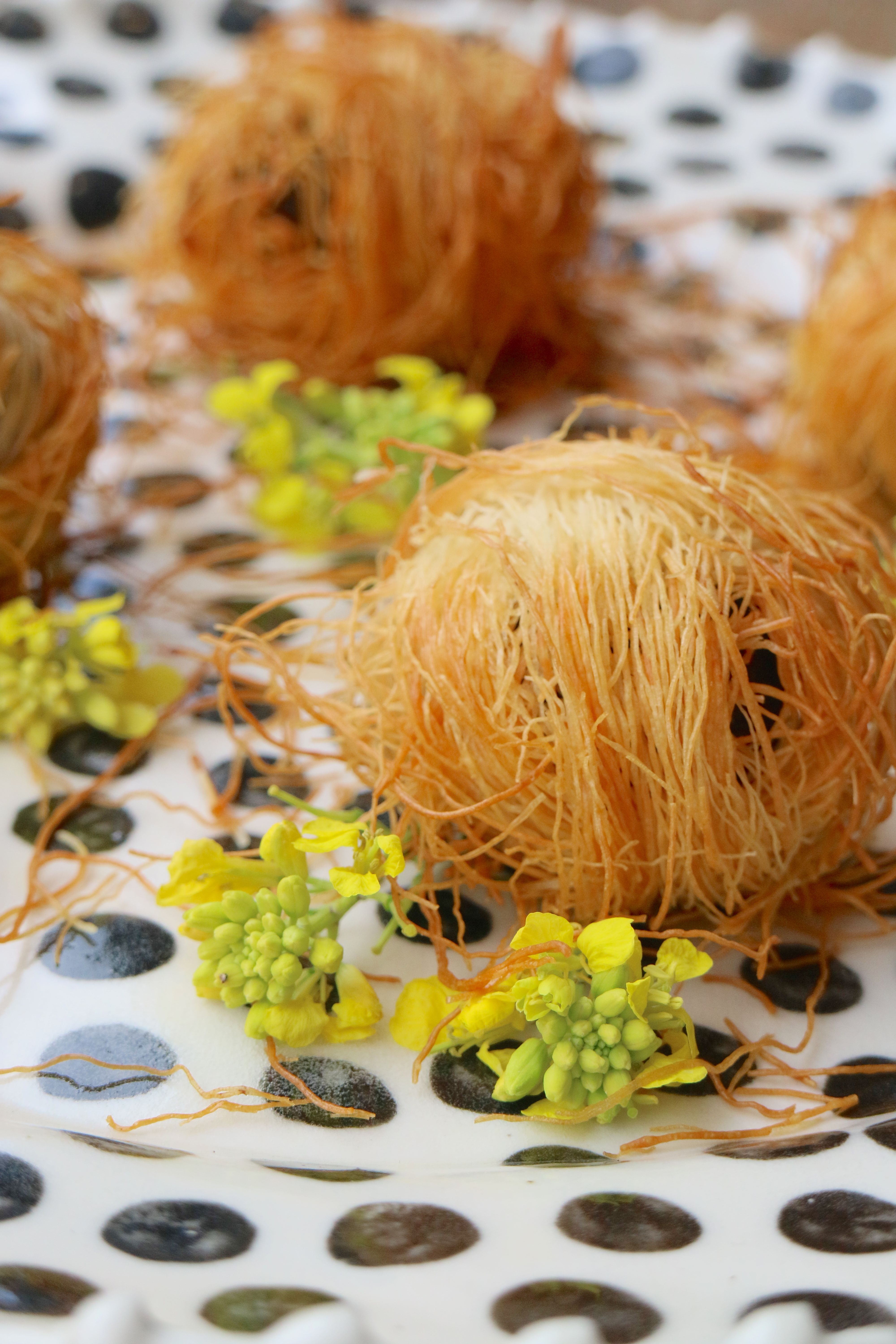 Golden-brown shredded pastry desserts with yellow flowers on a polka dot plate.
