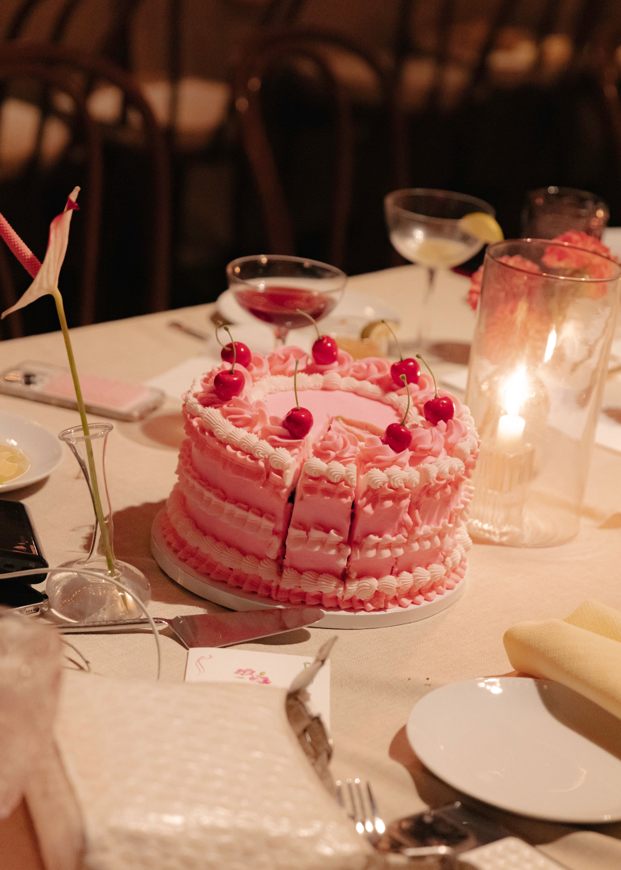 Elegant pink wedding cake with cherries displayed on a candlelit dessert table.