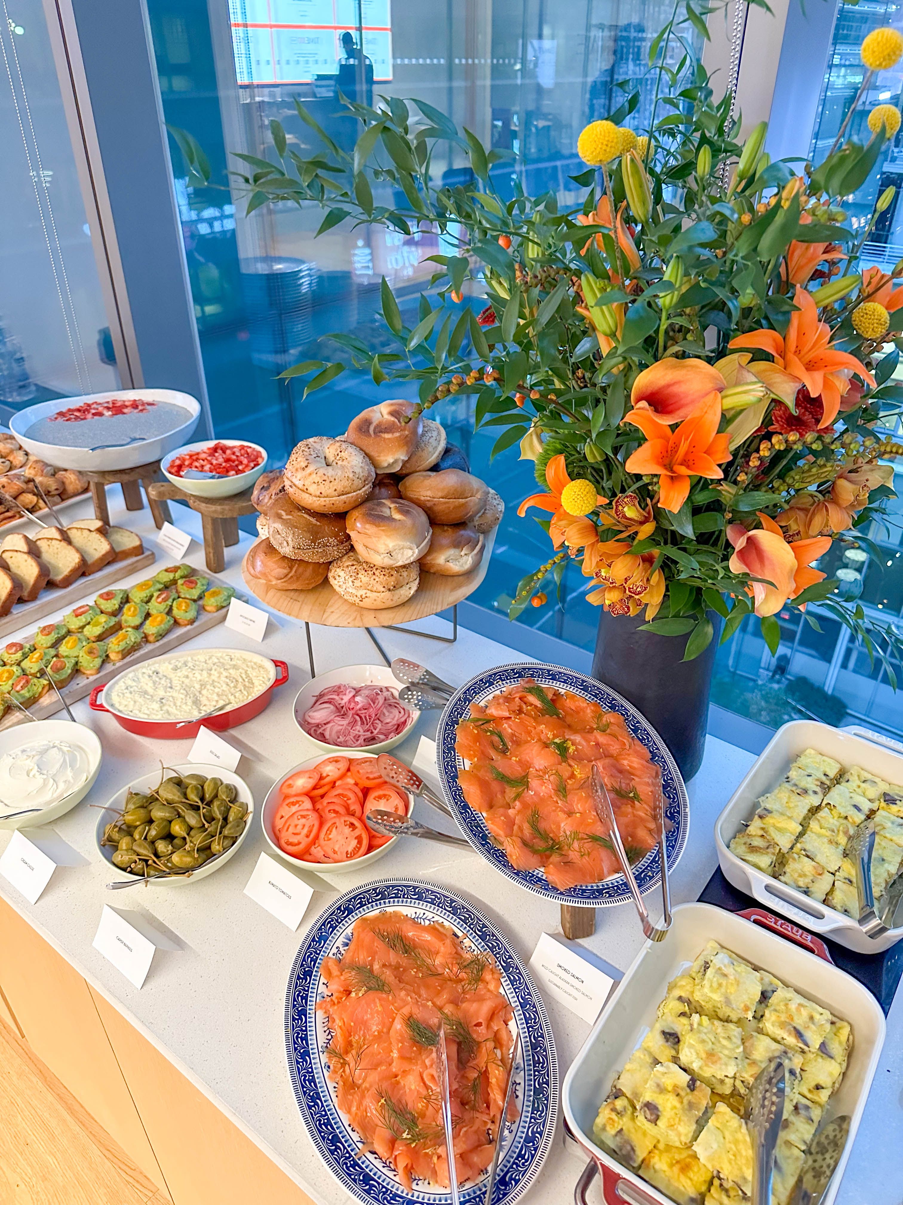 Catering bagel and smoked salmon brunch spread with cream cheese, tomatoes, capers, and fresh flowers.