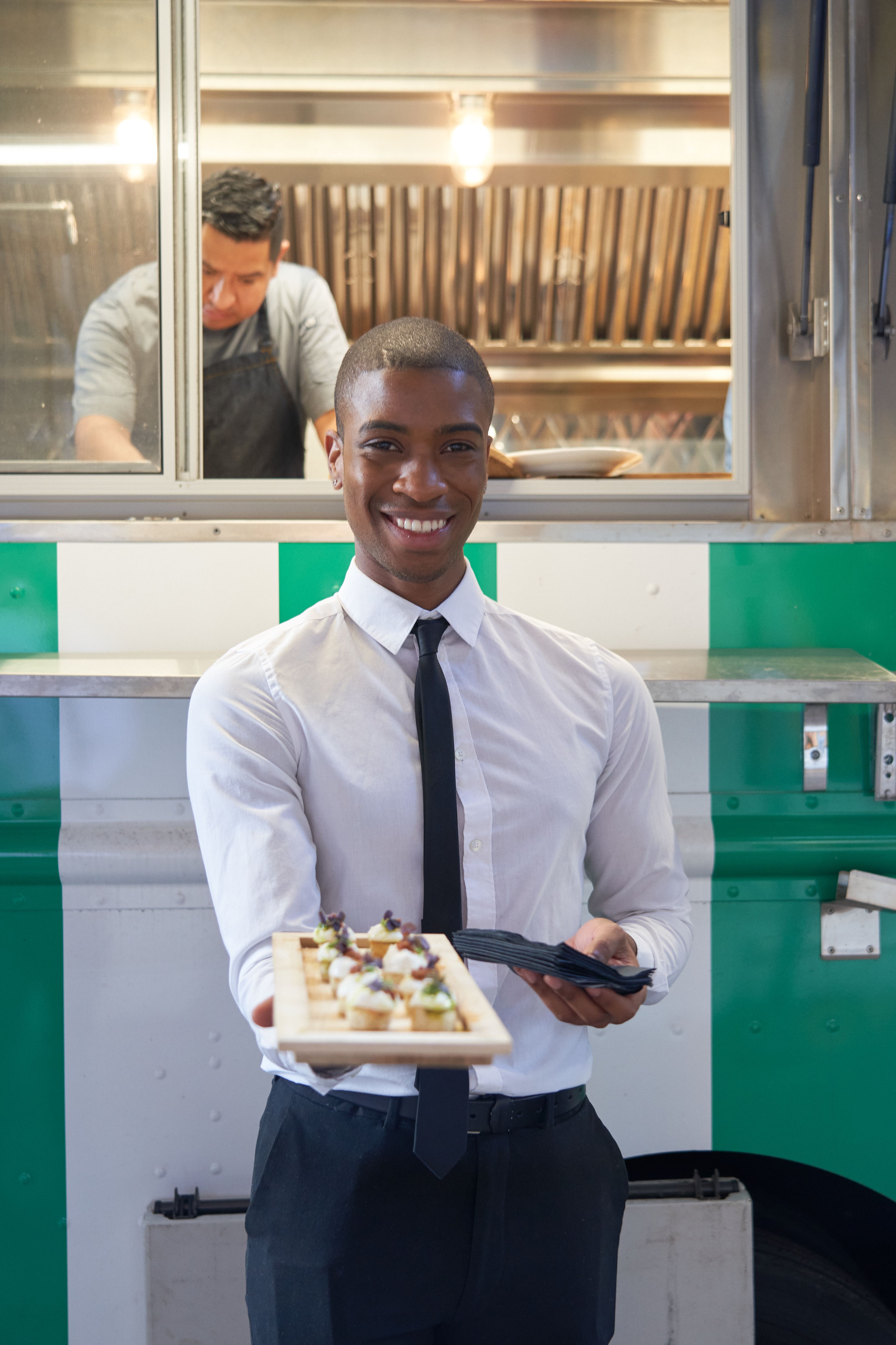 Catering server presenting canapés in front of a mobile kitchen truck at an event.