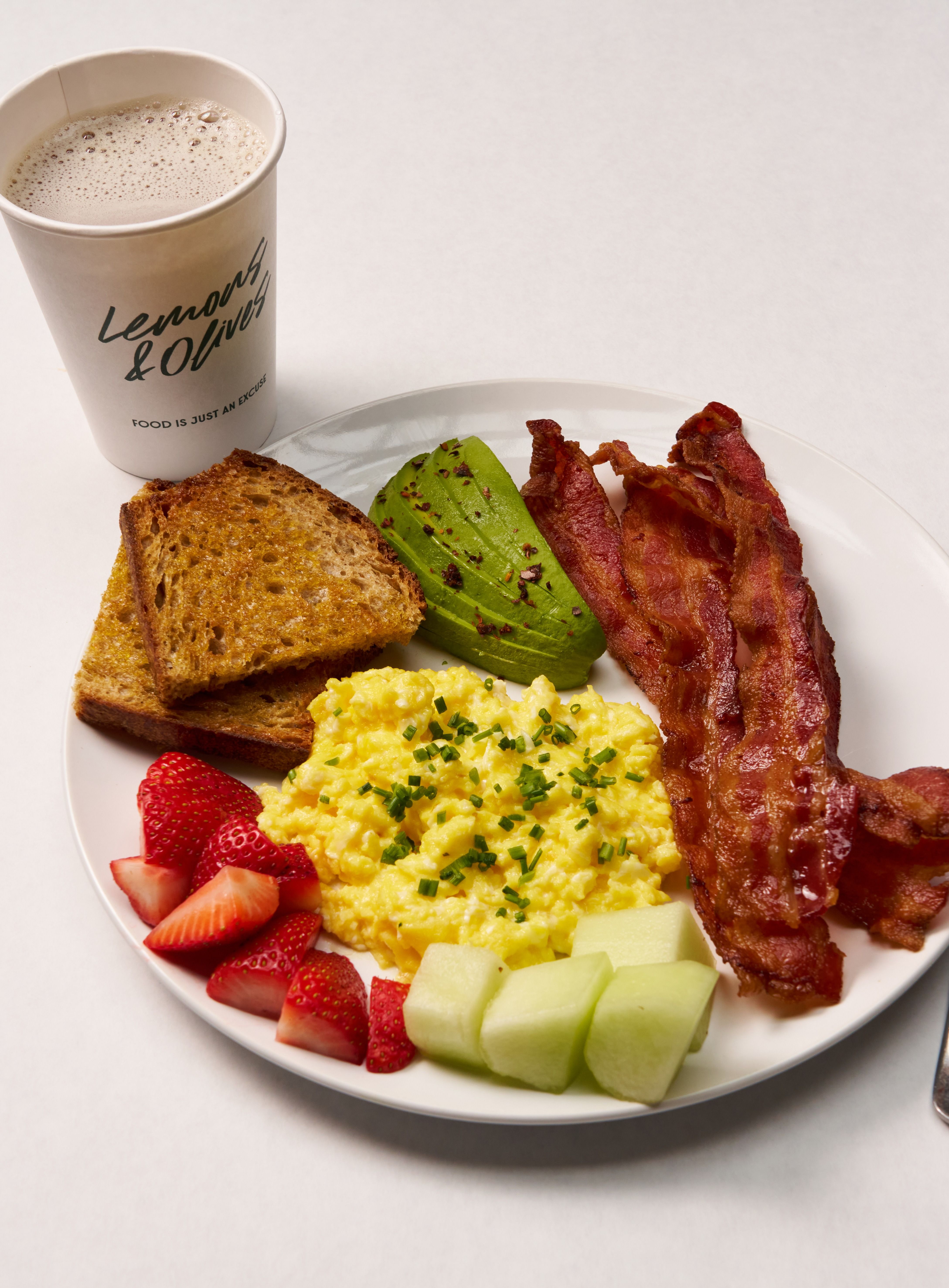 Breakfast plate with scrambled eggs, bacon, fruit and coffee.