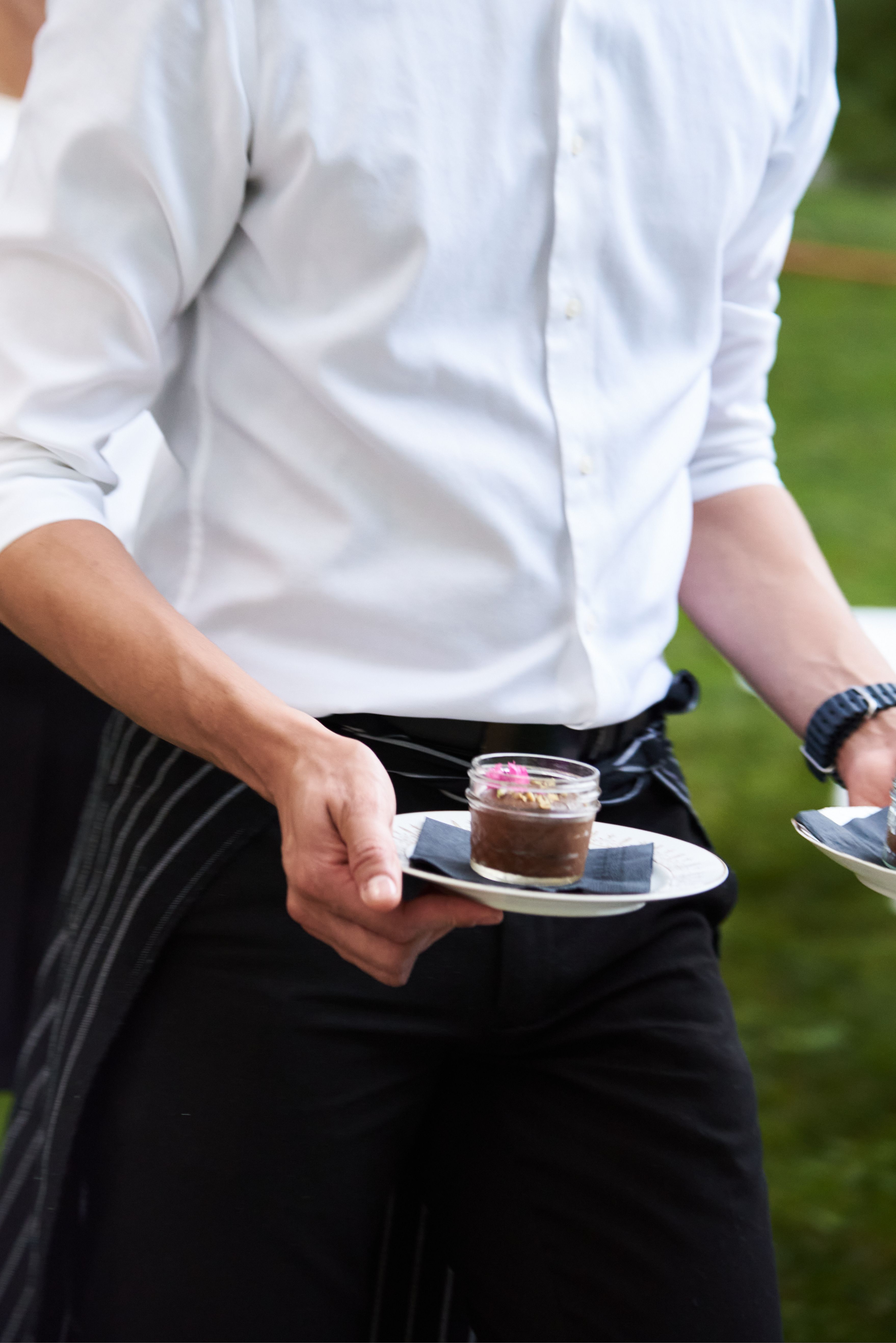 Server holding plated mini dessert bites during an outdoor catered event.