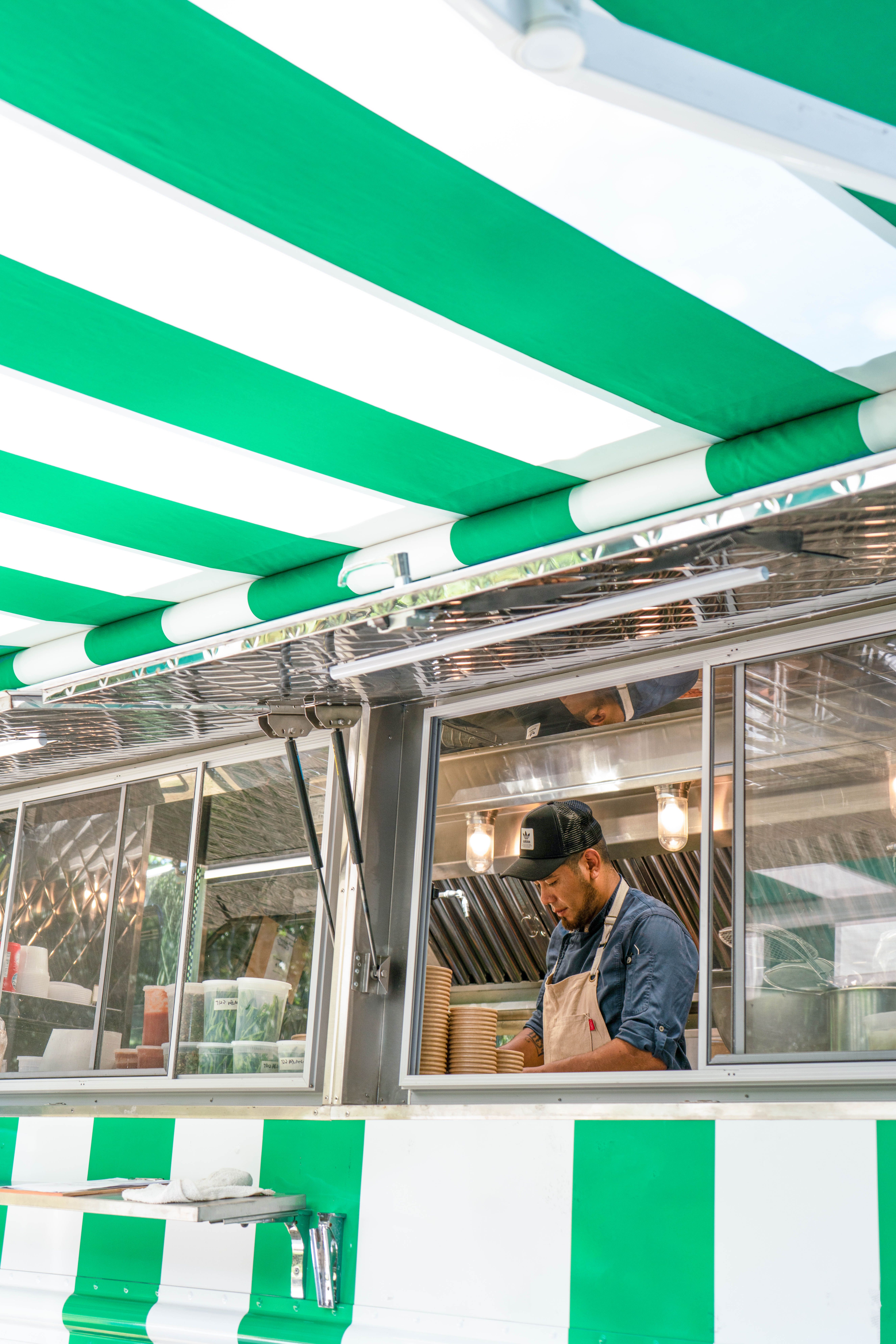 A man works inside a green and white striped food truck under a matching awning.