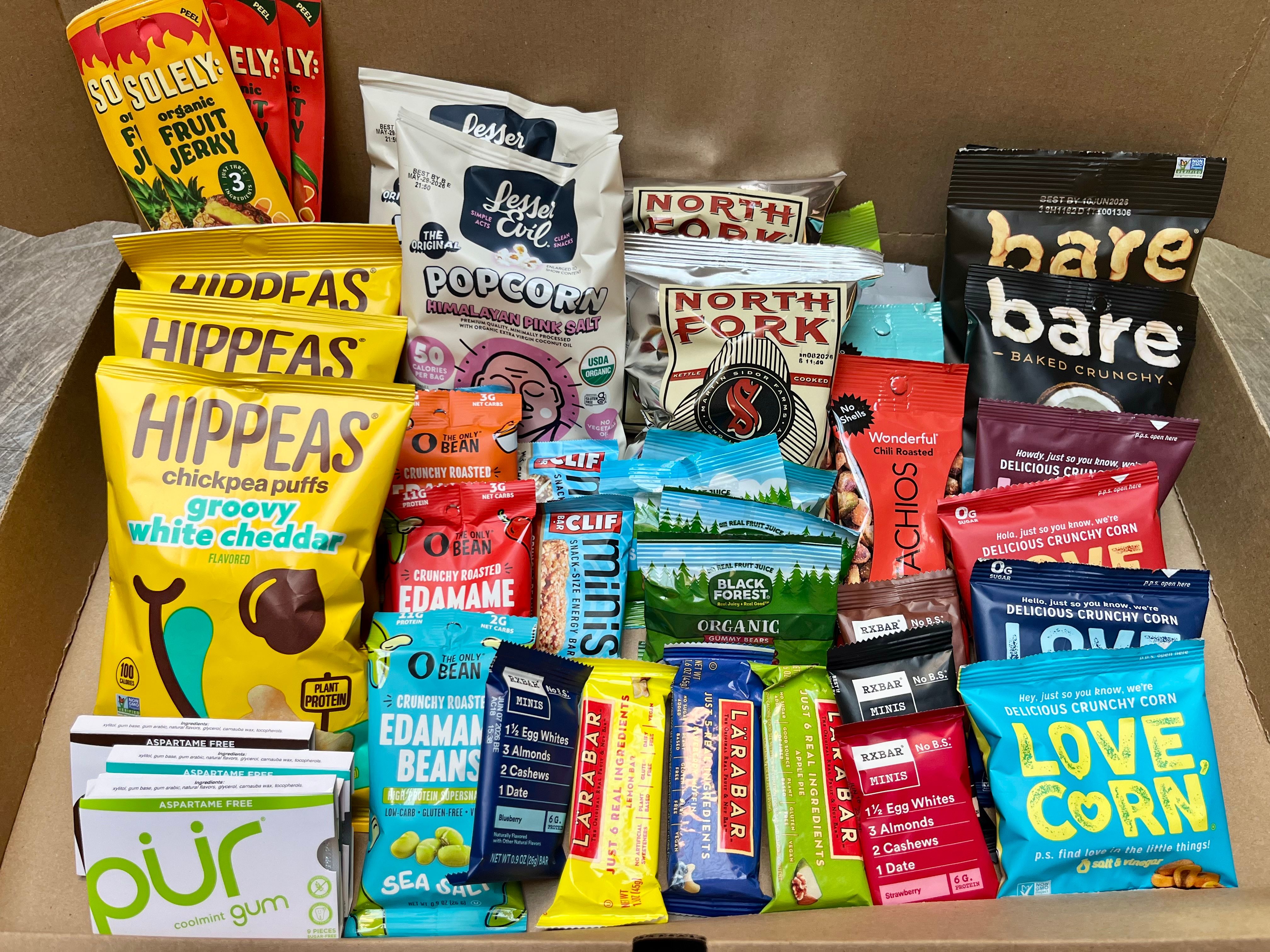 A cardboard box filled with an assortment of healthy snack foods and brands.