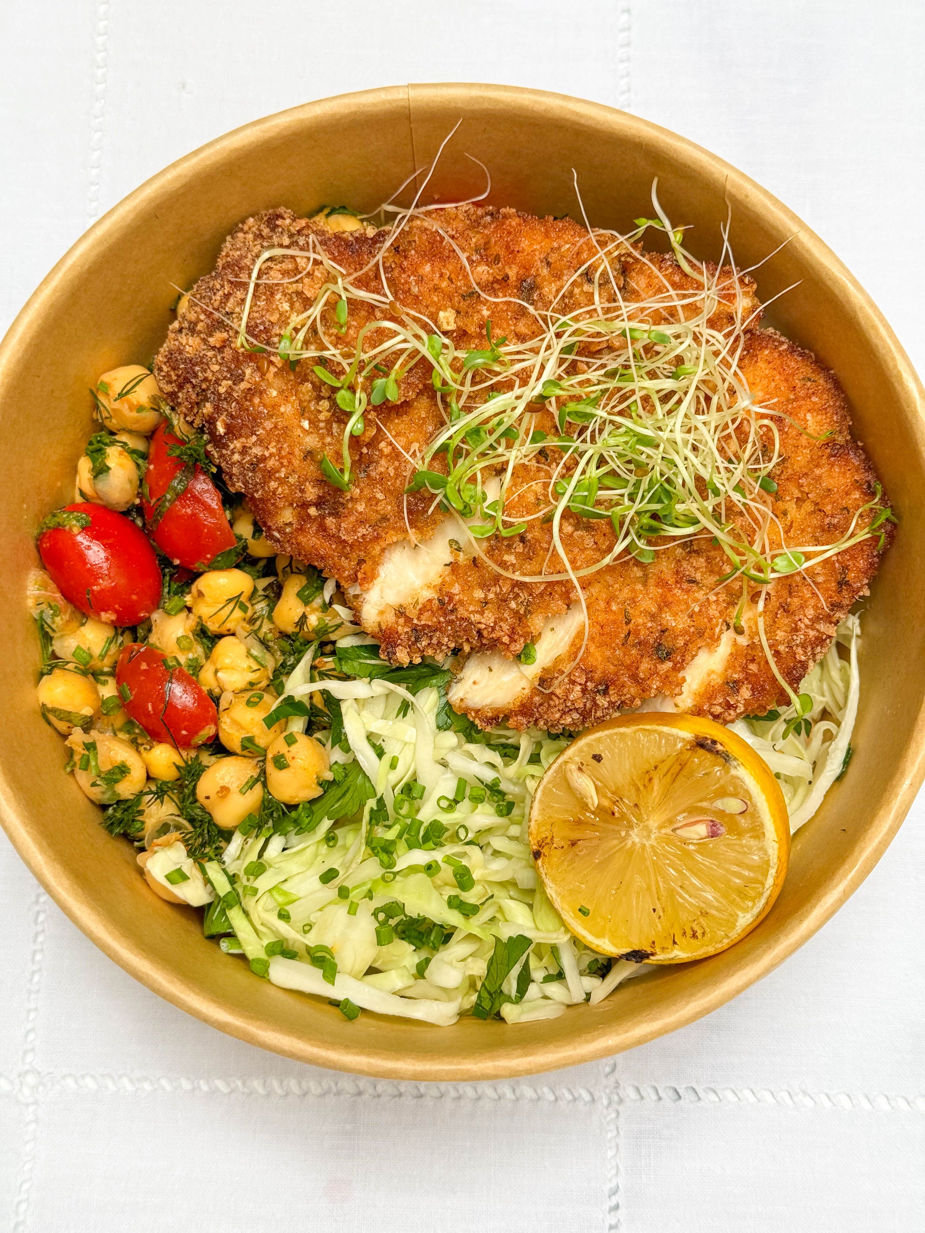 Catering crispy chicken salad bowl with chickpeas, cabbage slaw, tomatoes, and grilled lemon.