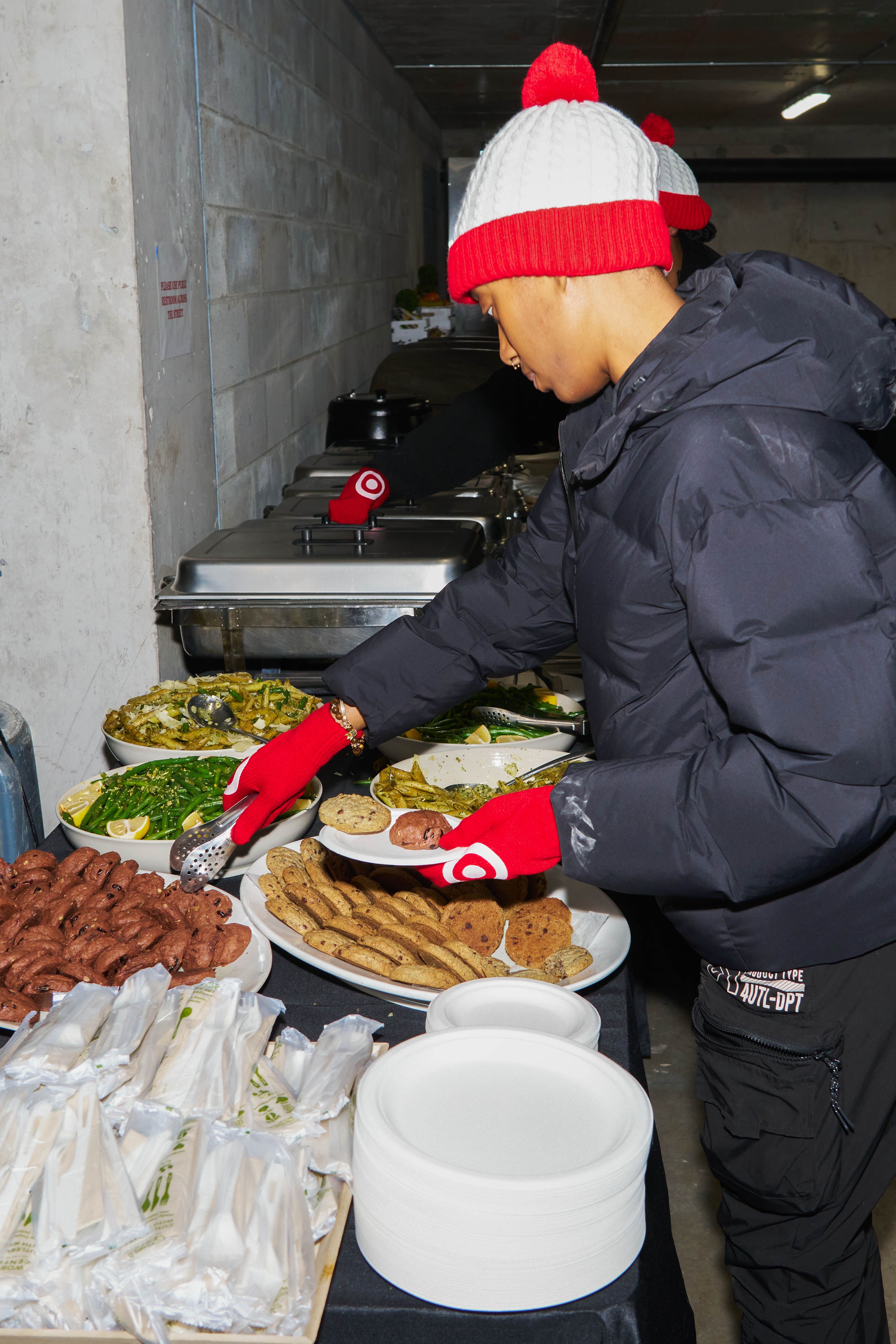 Guest selecting food from a catered buffet with vegetables and desserts at a winter event.
