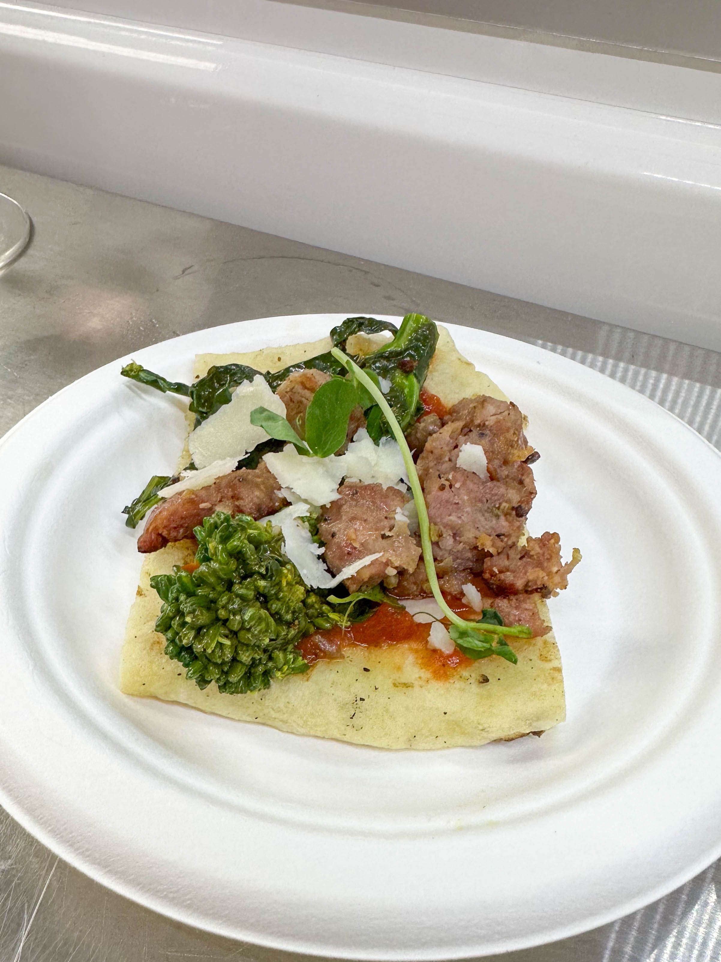 Gourmet flatbread appetizer topped with sausage, pesto, and shaved cheese served for event catering.