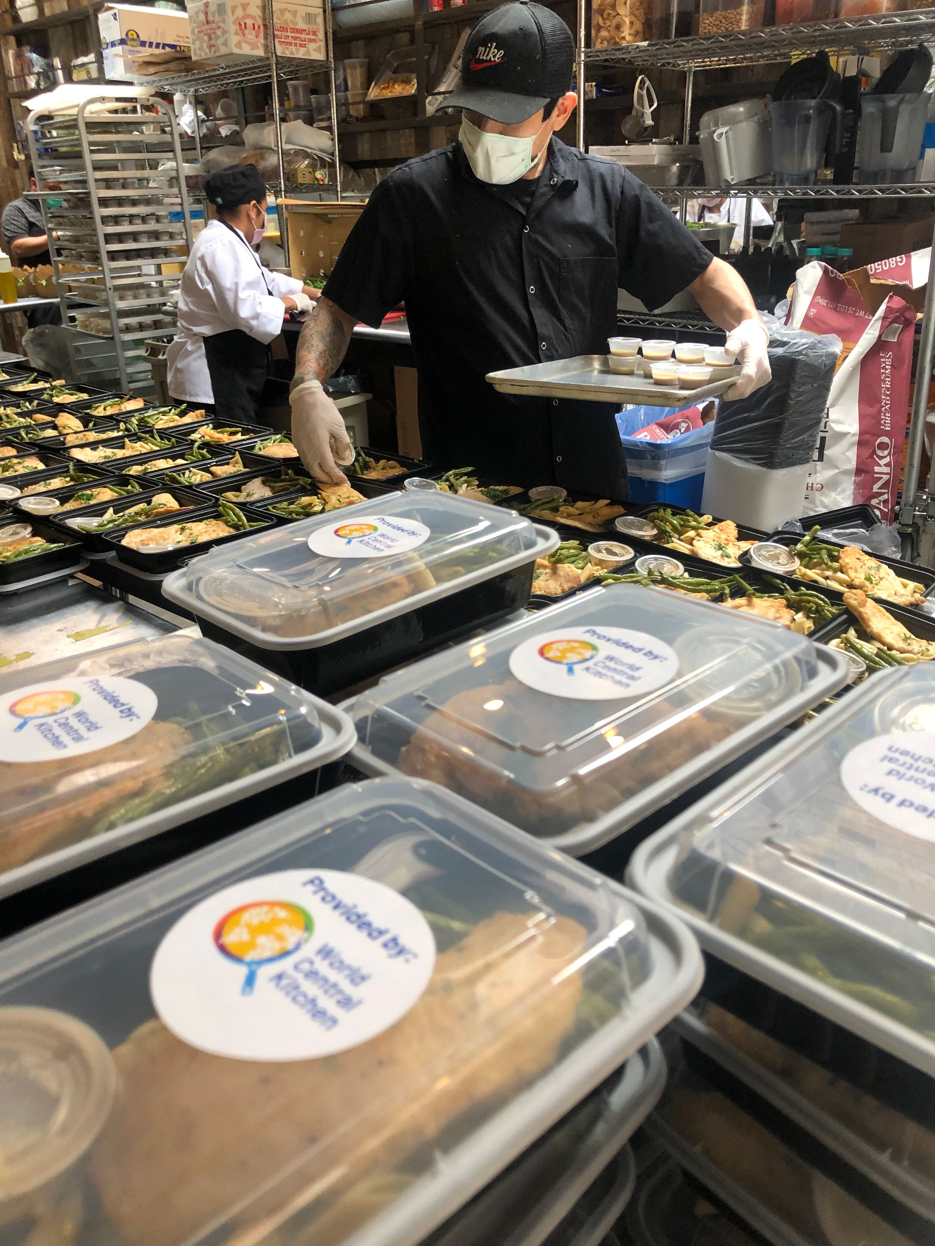 Catering staff preparing and packaging hot meals in a commercial kitchen for emergency response.