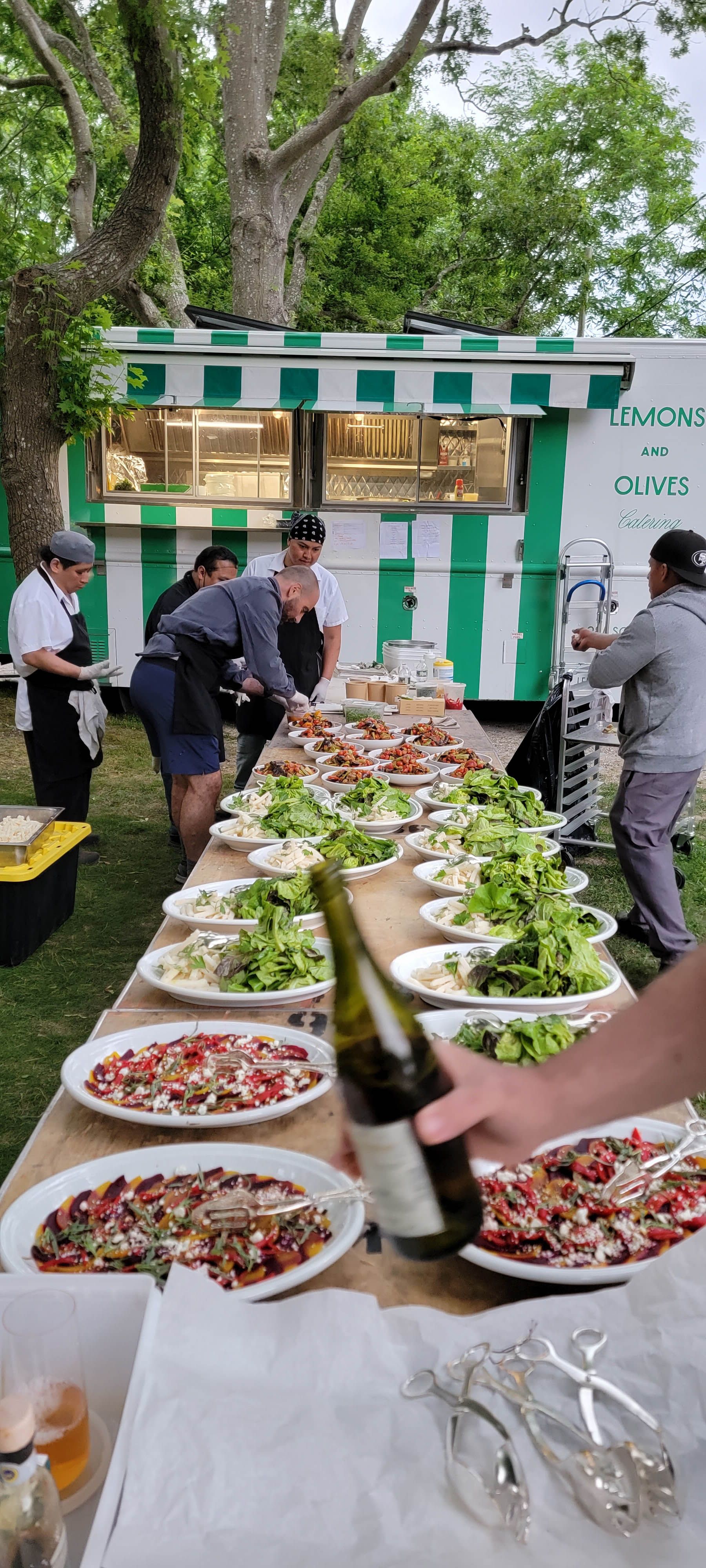 Lemons and Olives catering team preparing plated dishes at an outdoor wedding beside their catering food truck.