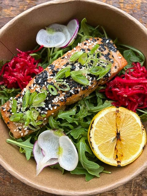 Catering sesame-crusted salmon salad bowl with arugula, pickled cabbage, radishes, and grilled lemon.