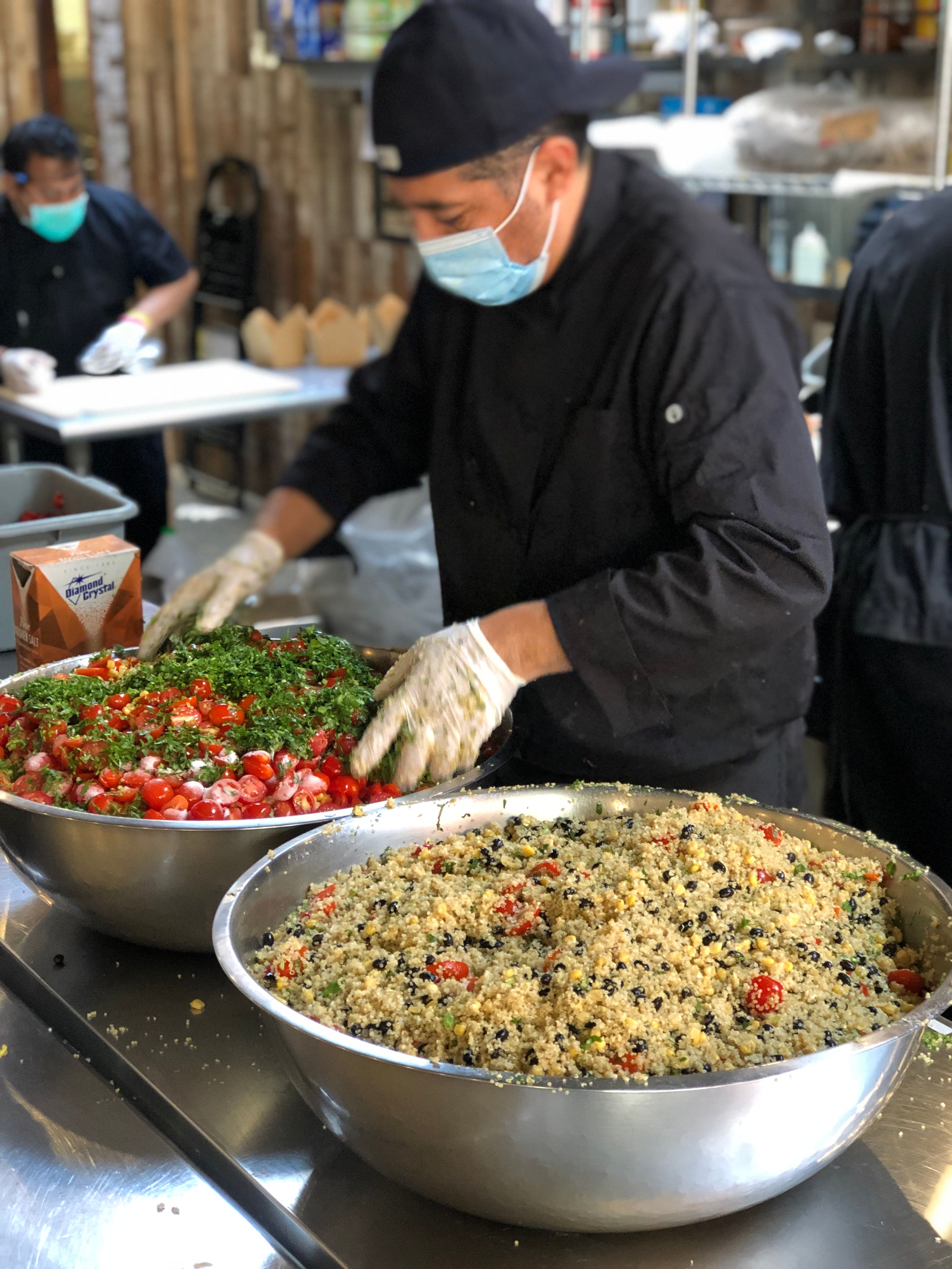 Chef preparing large batches of salad and grain dishes in a commercial kitchen for emergency food service.