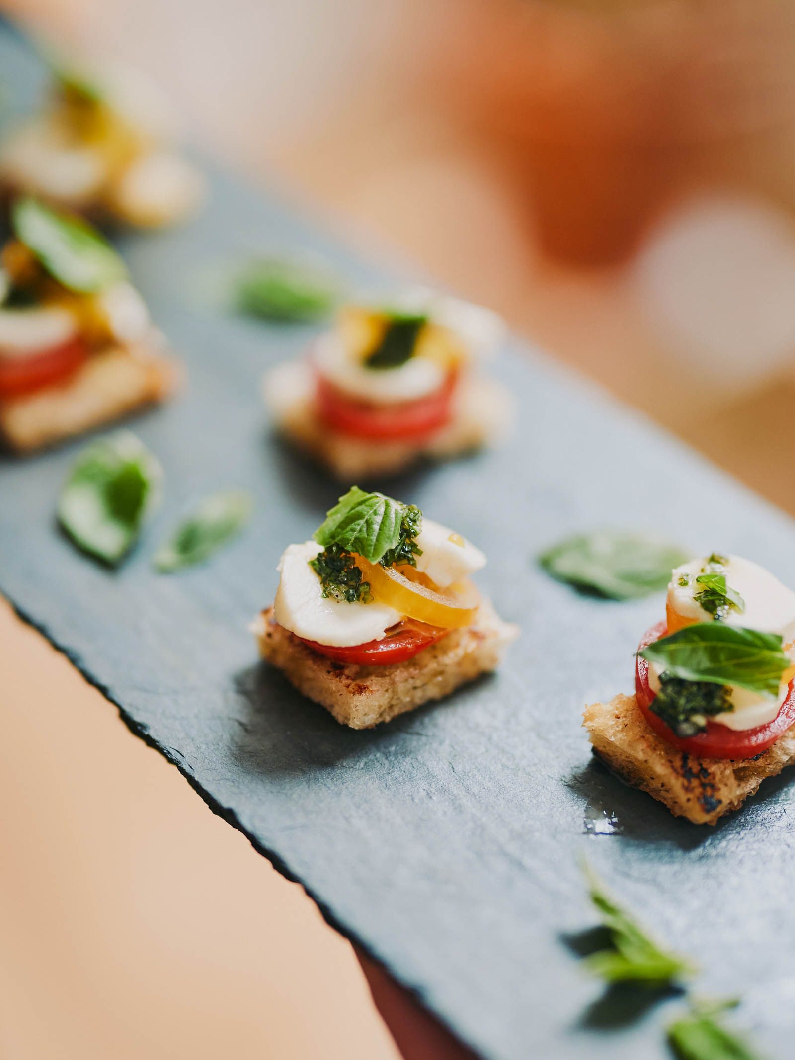 Elevated Hors d'oeuvres for corporate events with tomato, mozzarella, pesto, and basil on a slate board.