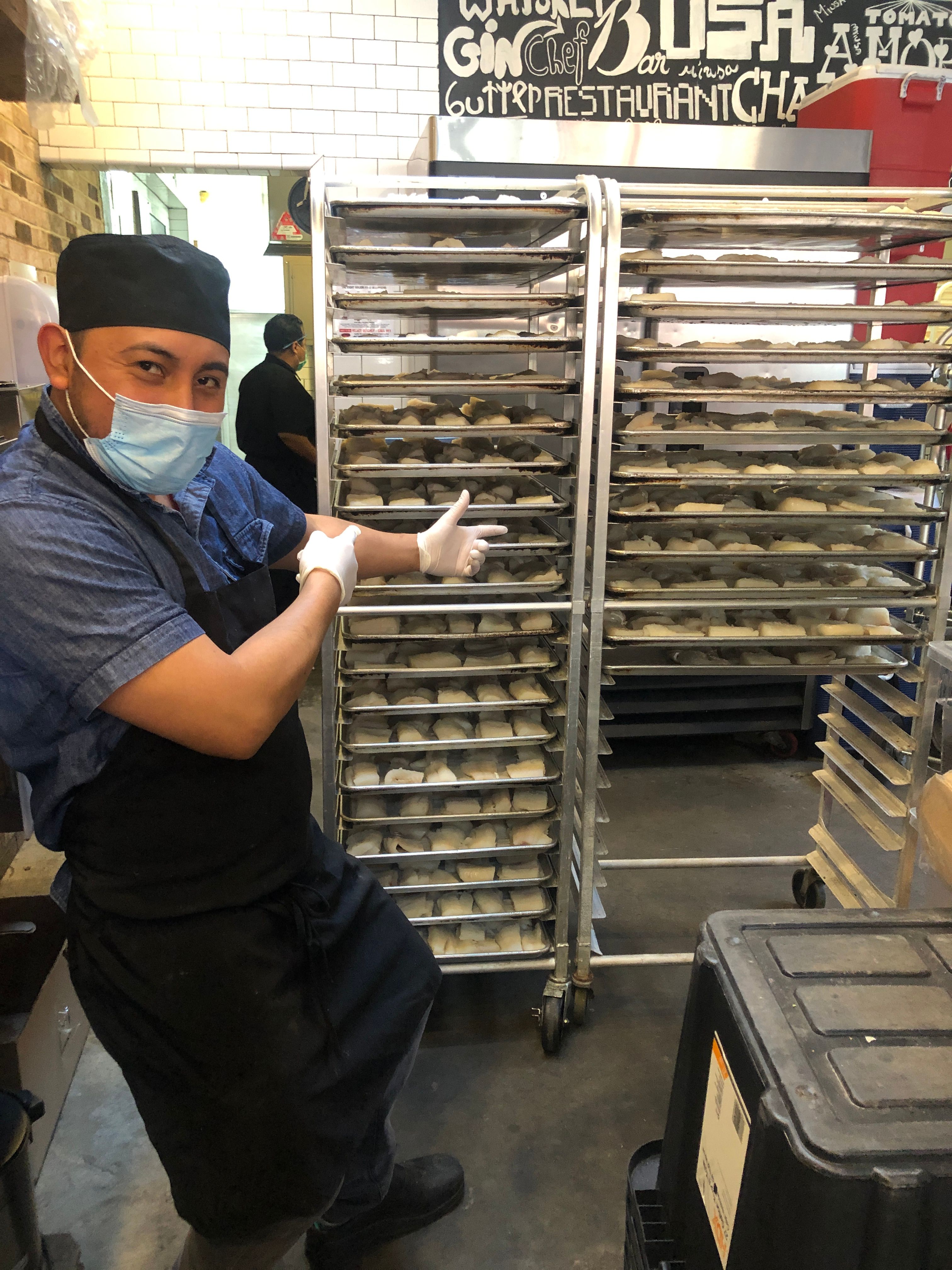 Chef standing beside trays of freshly prepared bread for large-scale emergency meal production.
