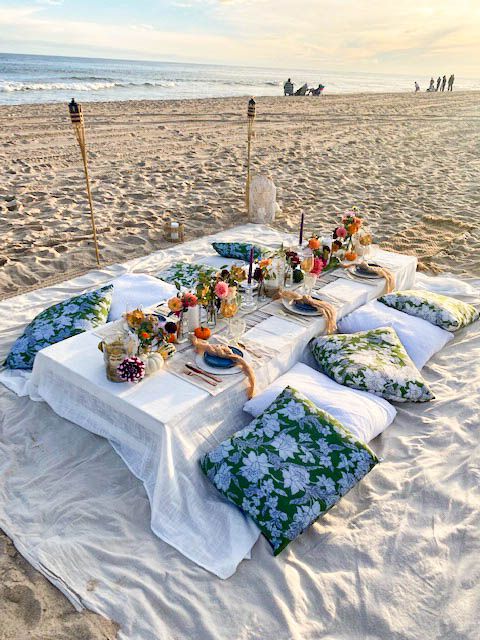 Elegant beach dinner setup with low table, floral decor, and cushions for a luxury catered event.