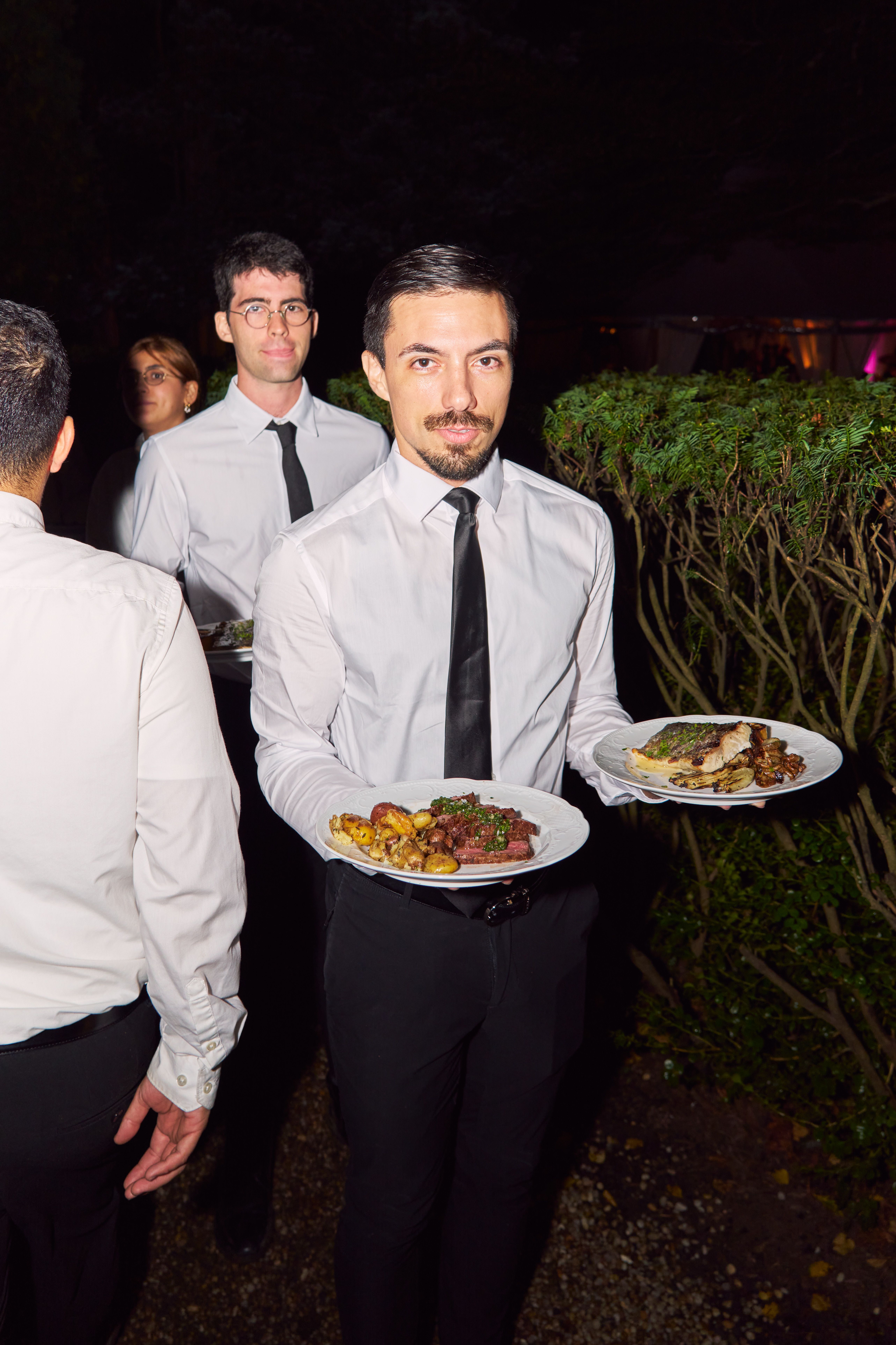 Professional catering staff serving plated dinner dishes at a wedding.
