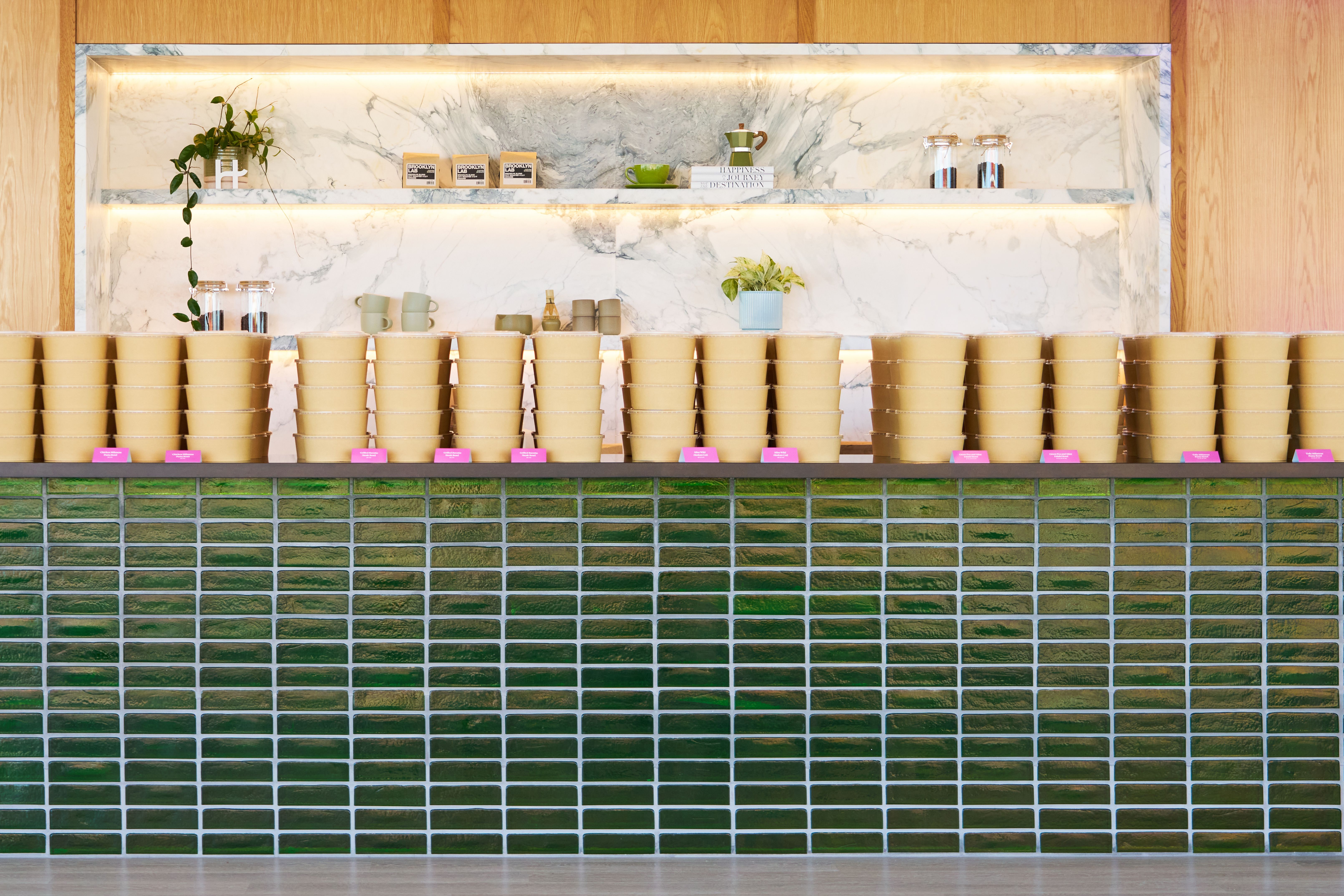 A counter with green subway tiles, topped with stacked bowls, backed by a marble wall and illuminated shelf.