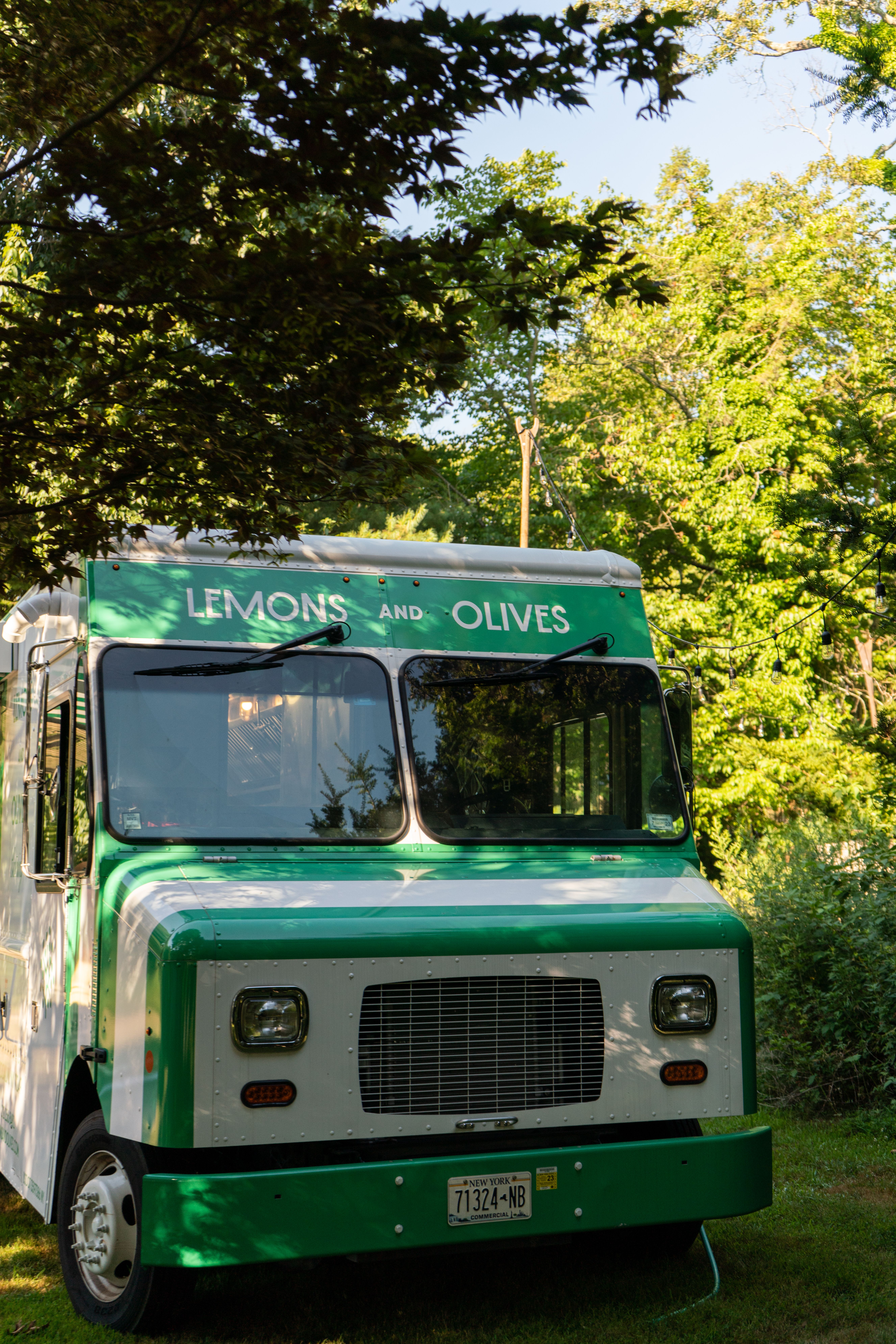 A green and white "Lemons and Olives" food truck parked outdoors among trees.