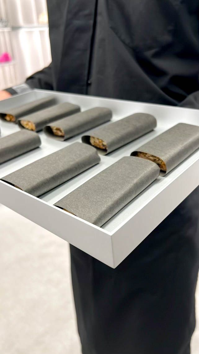 Server presenting minimalist black-wrapped appetizer bites at a luxury fashion brand experience event.