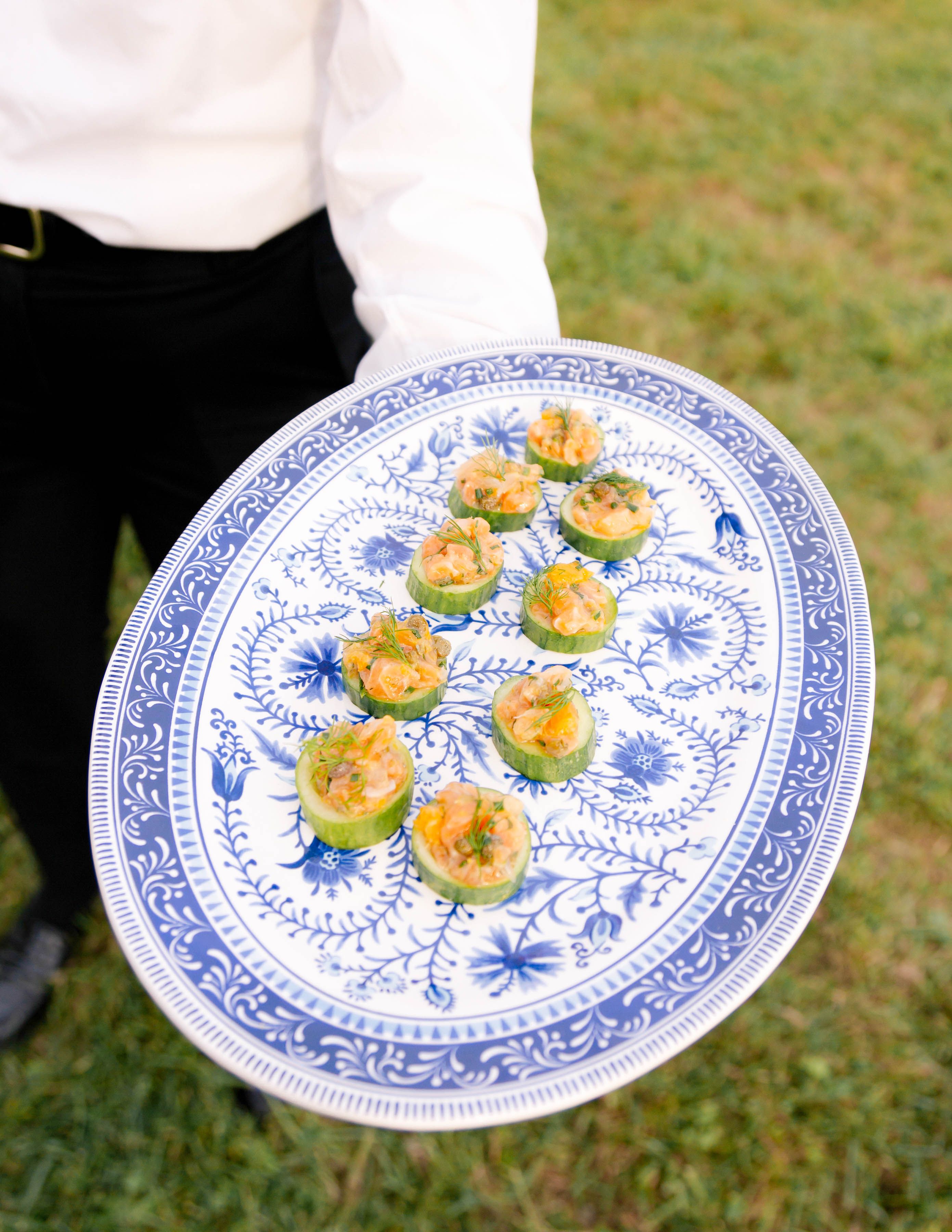 Catering server presenting passed wedding appetizers on a decorative platter.