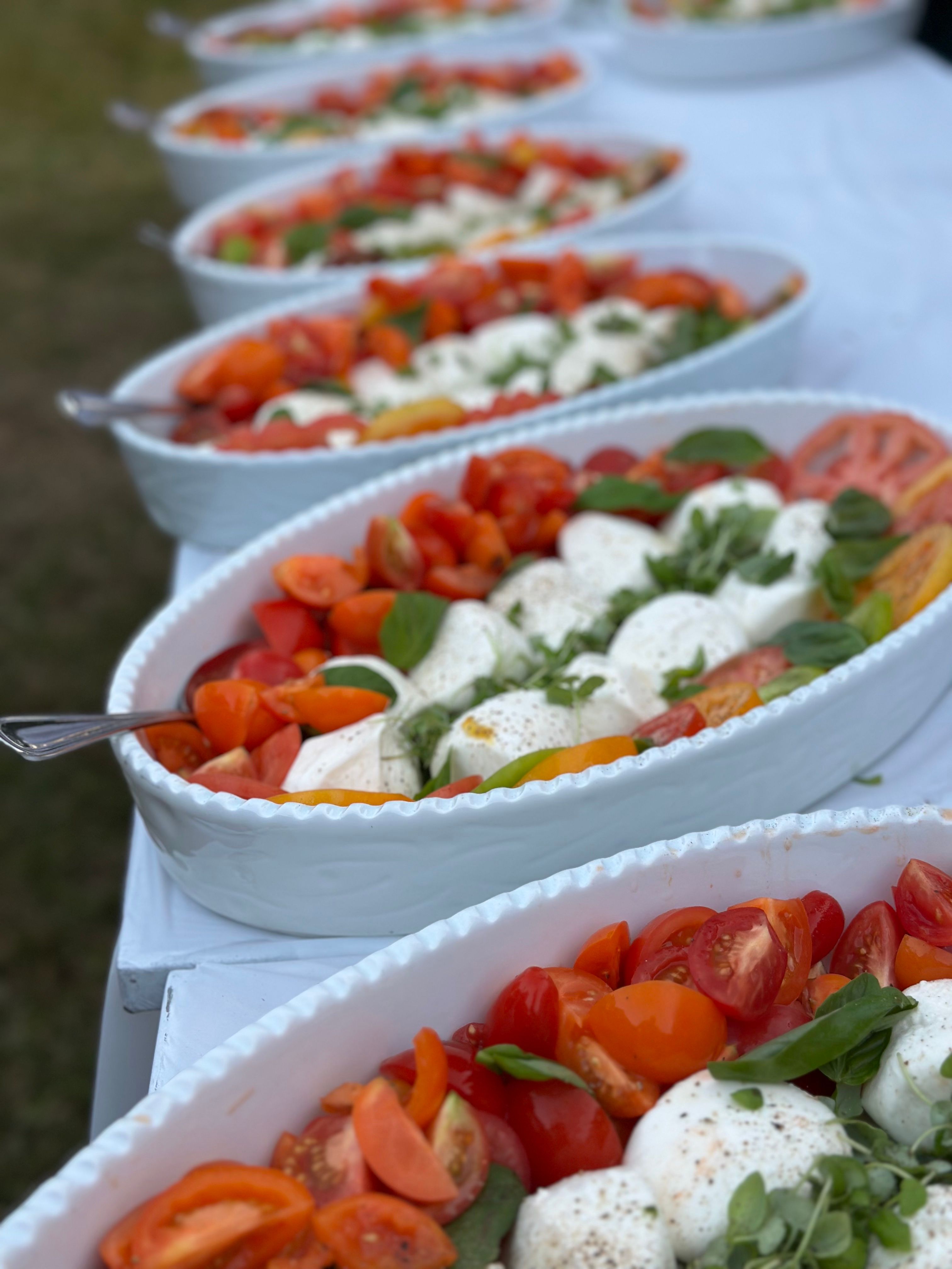 Caprese salad catering display with fresh mozzarella, tomatoes, and basil arranged in serving bowls at an outdoor event.