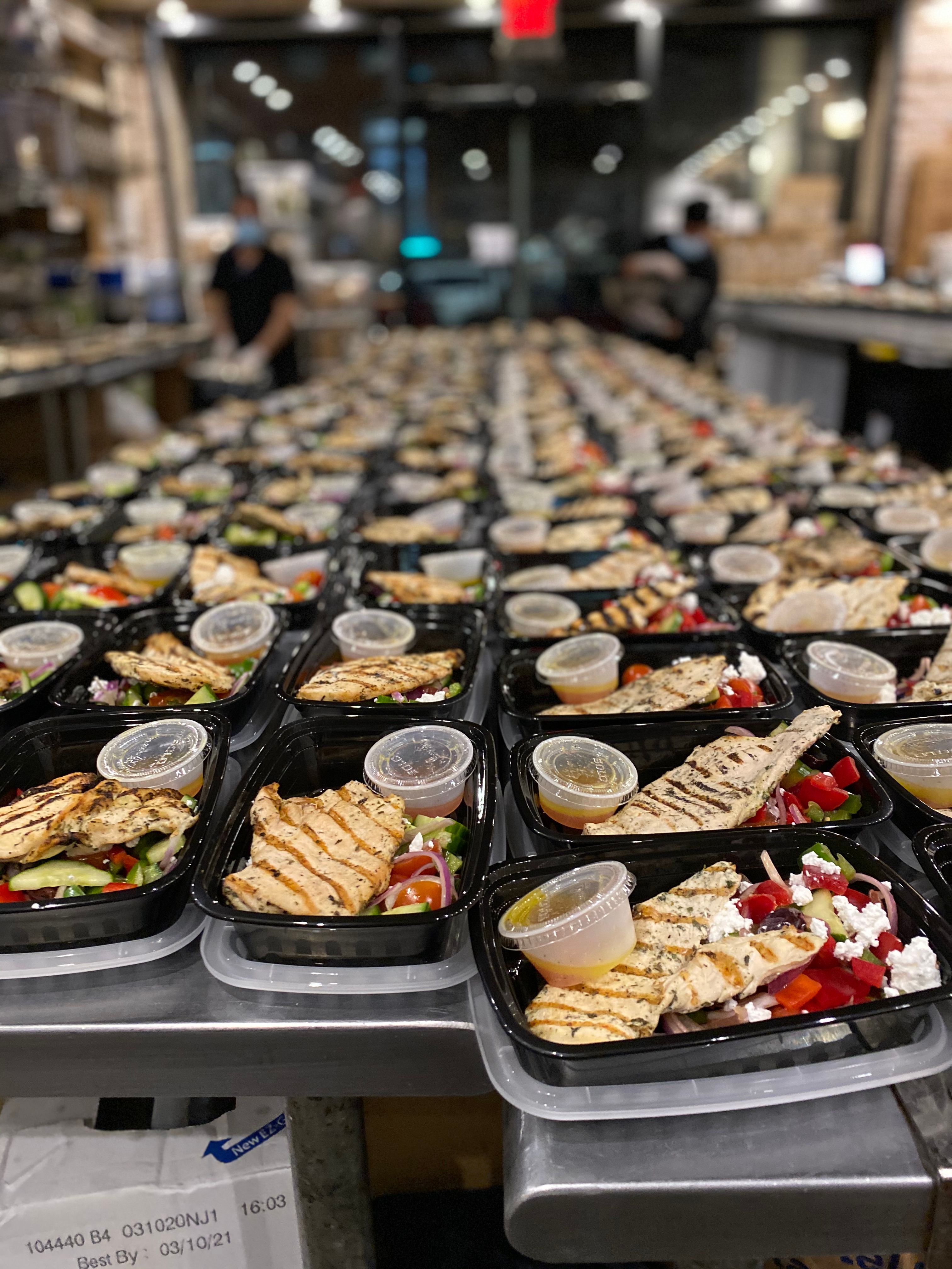Hundreds of packaged meals prepared on tables in a commercial kitchen for emergency food service operations.