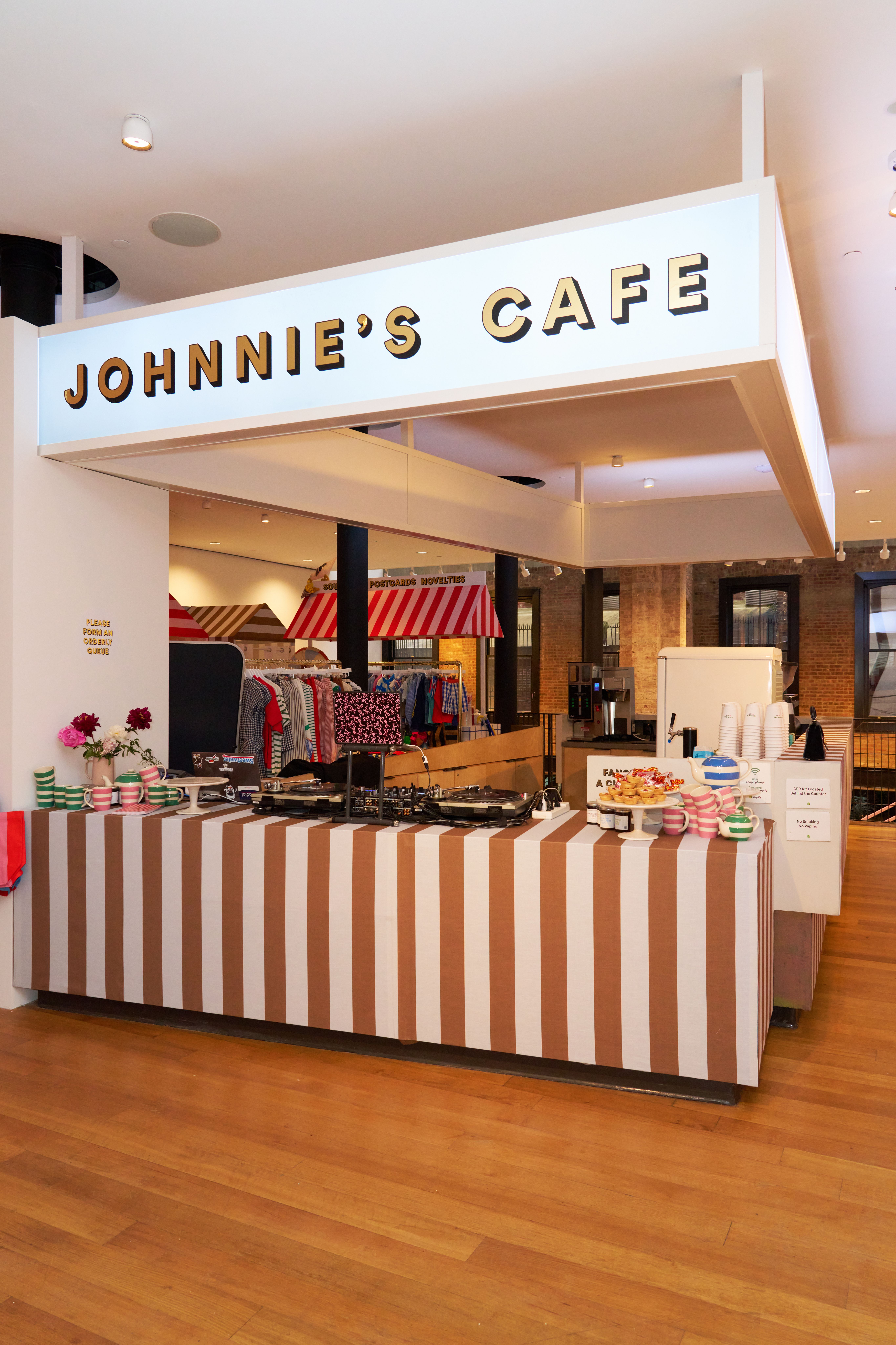 "Johnie's Cafe" sign above a brown and white striped counter with pastries, drinks, and a DJ setup.