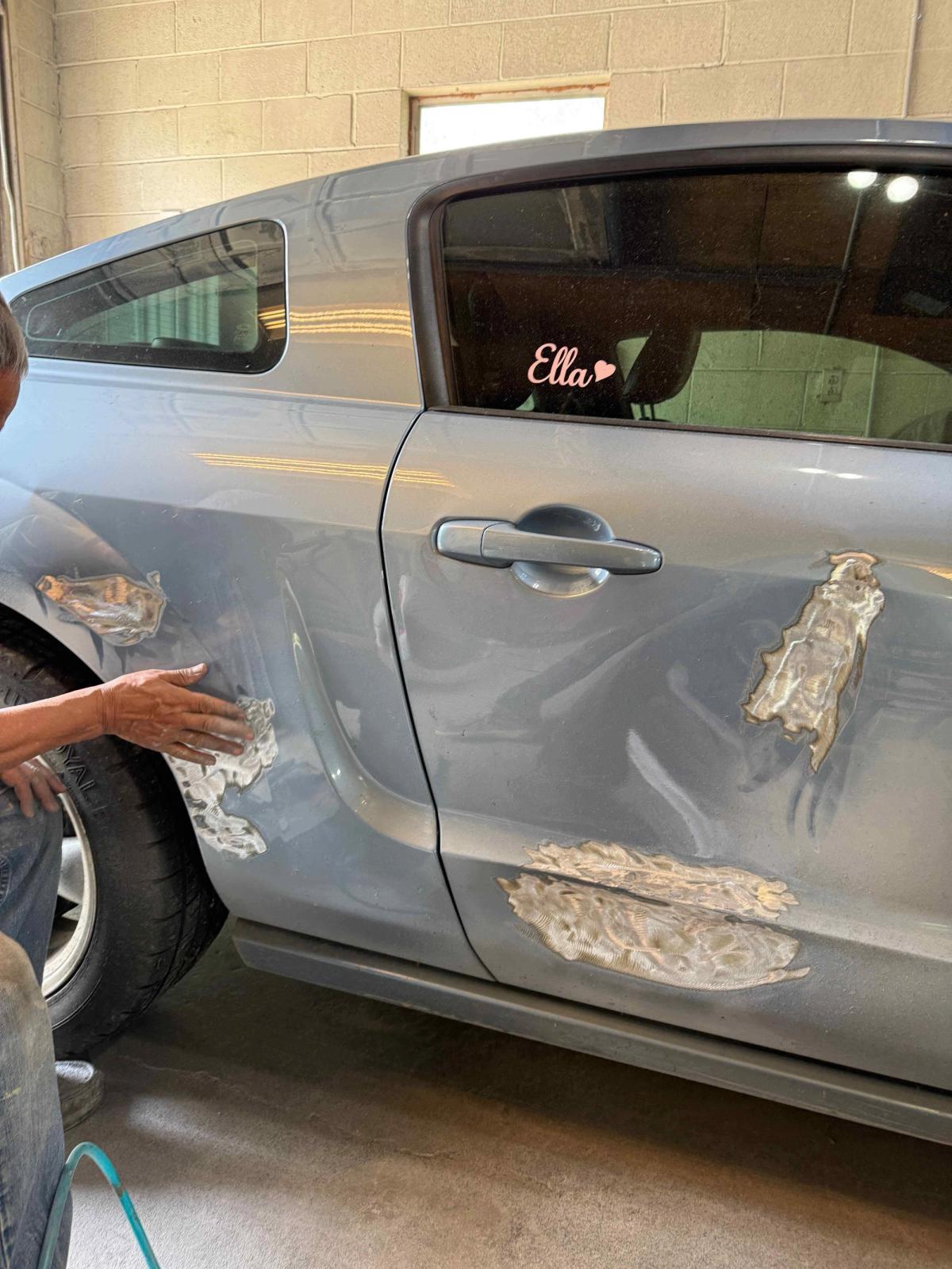 Dented car door mid-repair with damaged sheet metal pulled back into shape