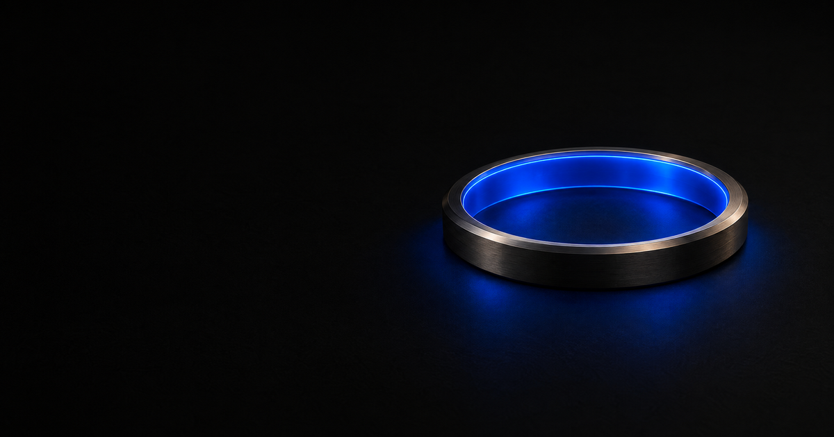 A machined reference ring of dark metal lies flat on a black floor, seen from high and off to one side, with one unbroken blue cobalt charge running the full inner wall and a matching cobalt spill pooling on the floor around it.
