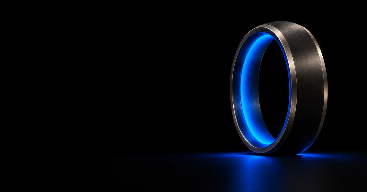 A dark machined metal ring standing upright and turned at an angle, seen from slightly below, with one unbroken blue cobalt charge running its full inner edge and glowing onto the black floor beneath it.
