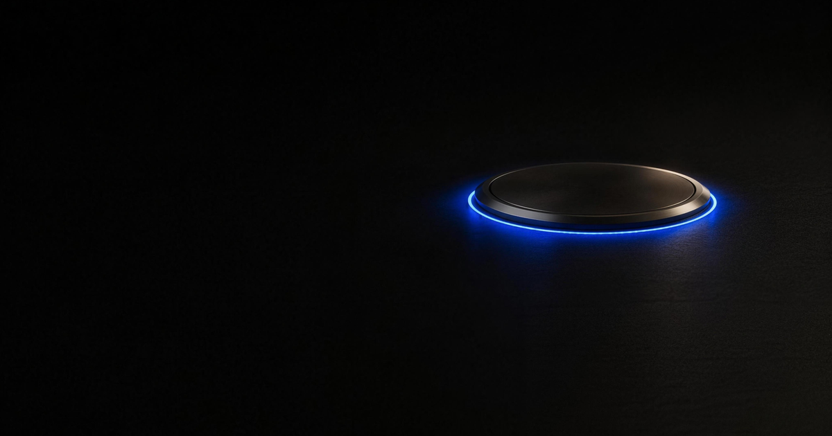 A single machined plate of dark metal seated in a black floor and standing slightly proud of it, seen from a distance, with one unbroken blue cobalt charge running the full seam around its edge and spilling onto the floor beneath it.