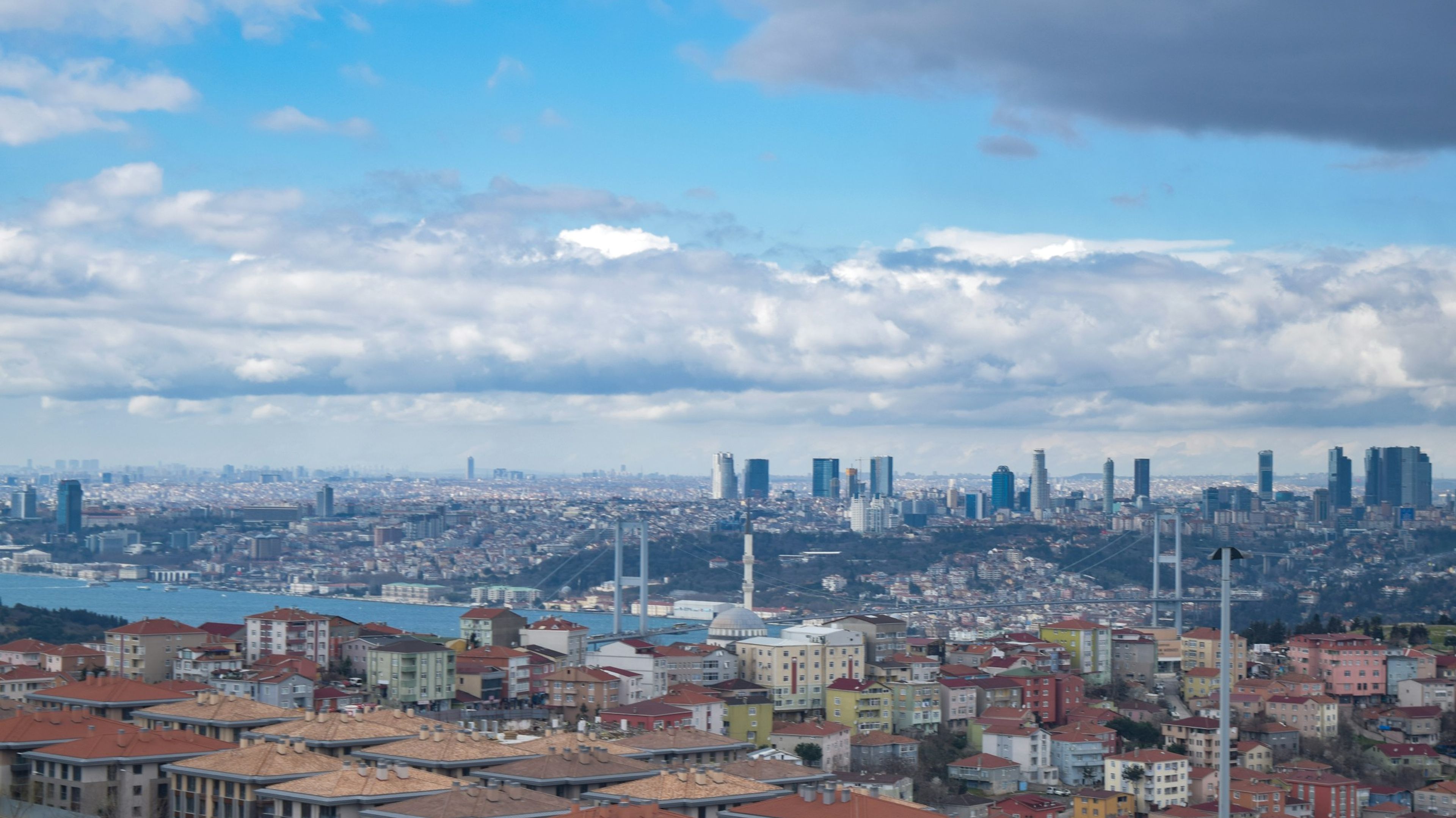 Boğaz köprüsü ve iki yakadaki konut dokusu, bulutlu gökyüzü altında