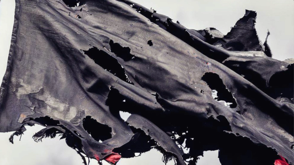A tattered, bloody black flag waves in the daylight.