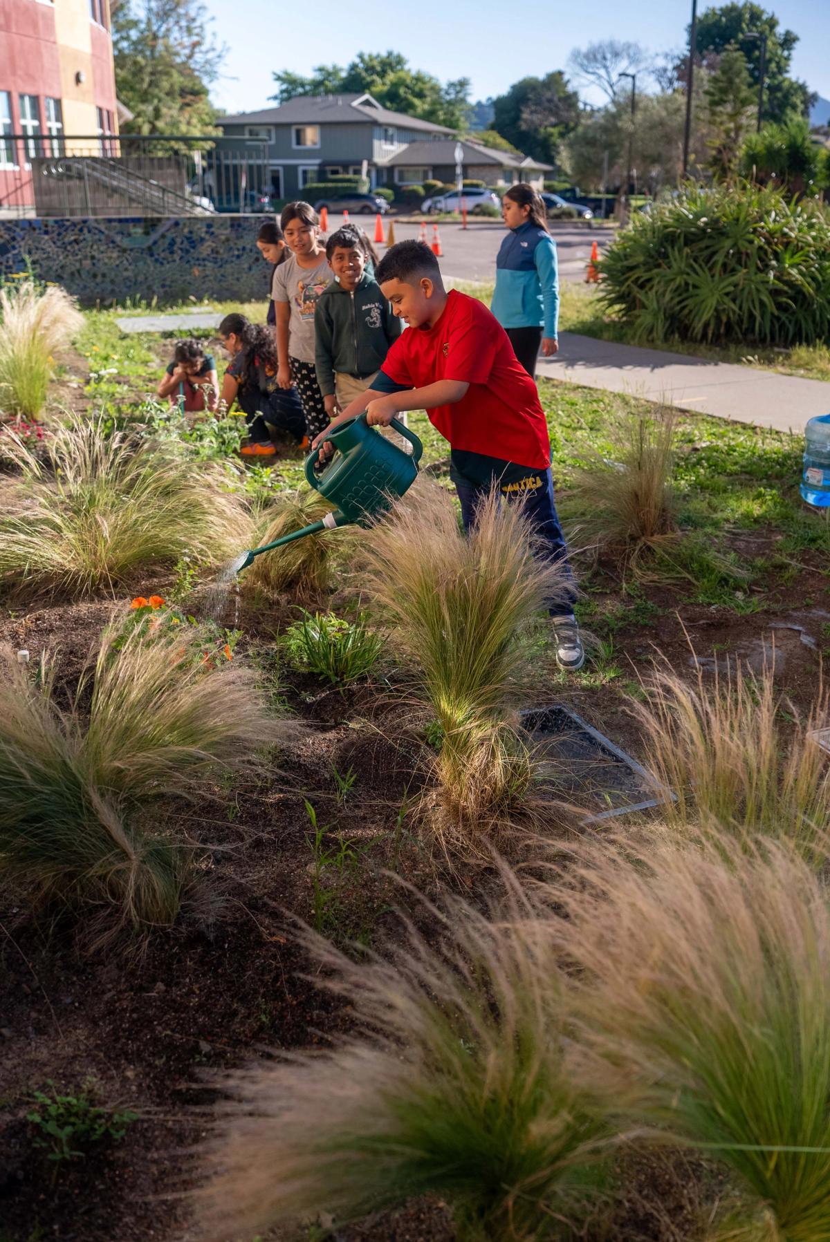 A student in a red shirt watering plants alongside classmates and instructors
