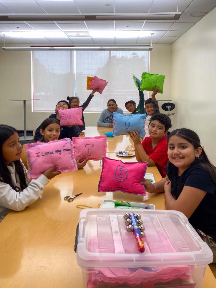 Students holding colorful finished pillows around a classroom table