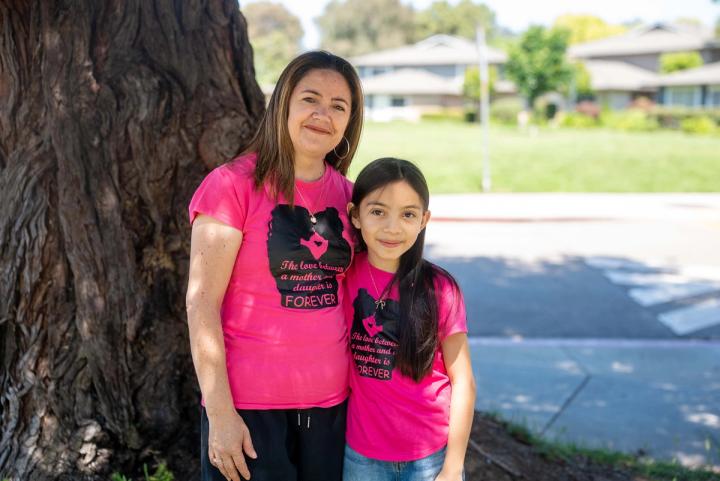 An adult and child smiling together beside a tree