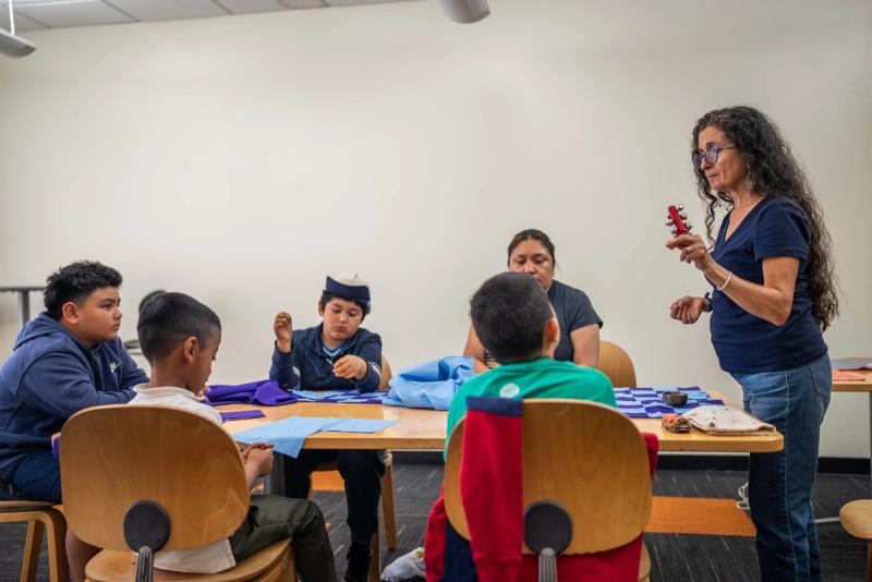 An instructor and a small group of students gathered around classroom tables