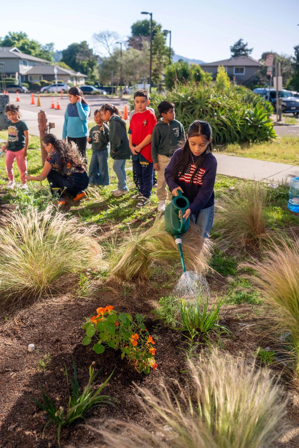 A student using a green watering can while the group works in the garden